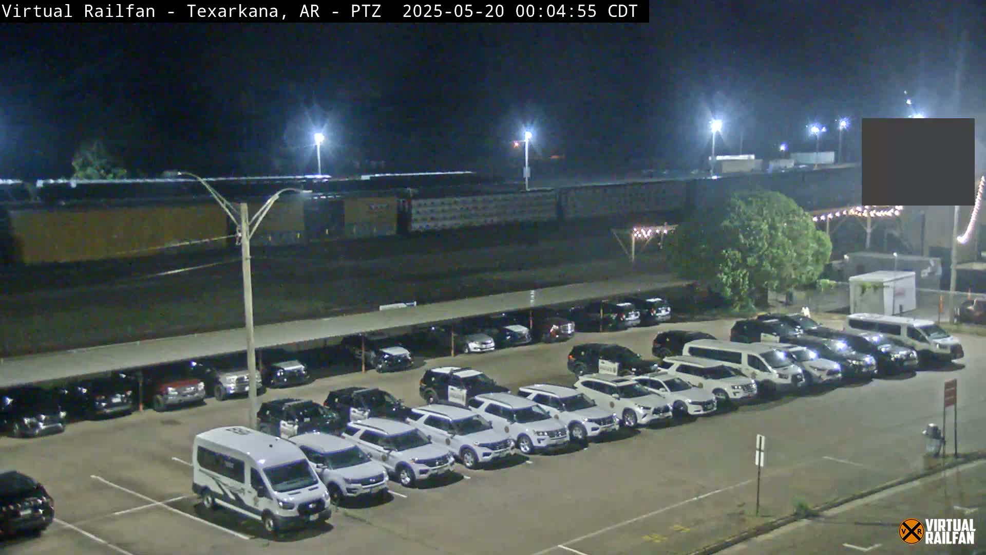 A nighttime parking lot filled with numerous cars, many of which are white SUVs, under covered and uncovered areas, next to a large building.