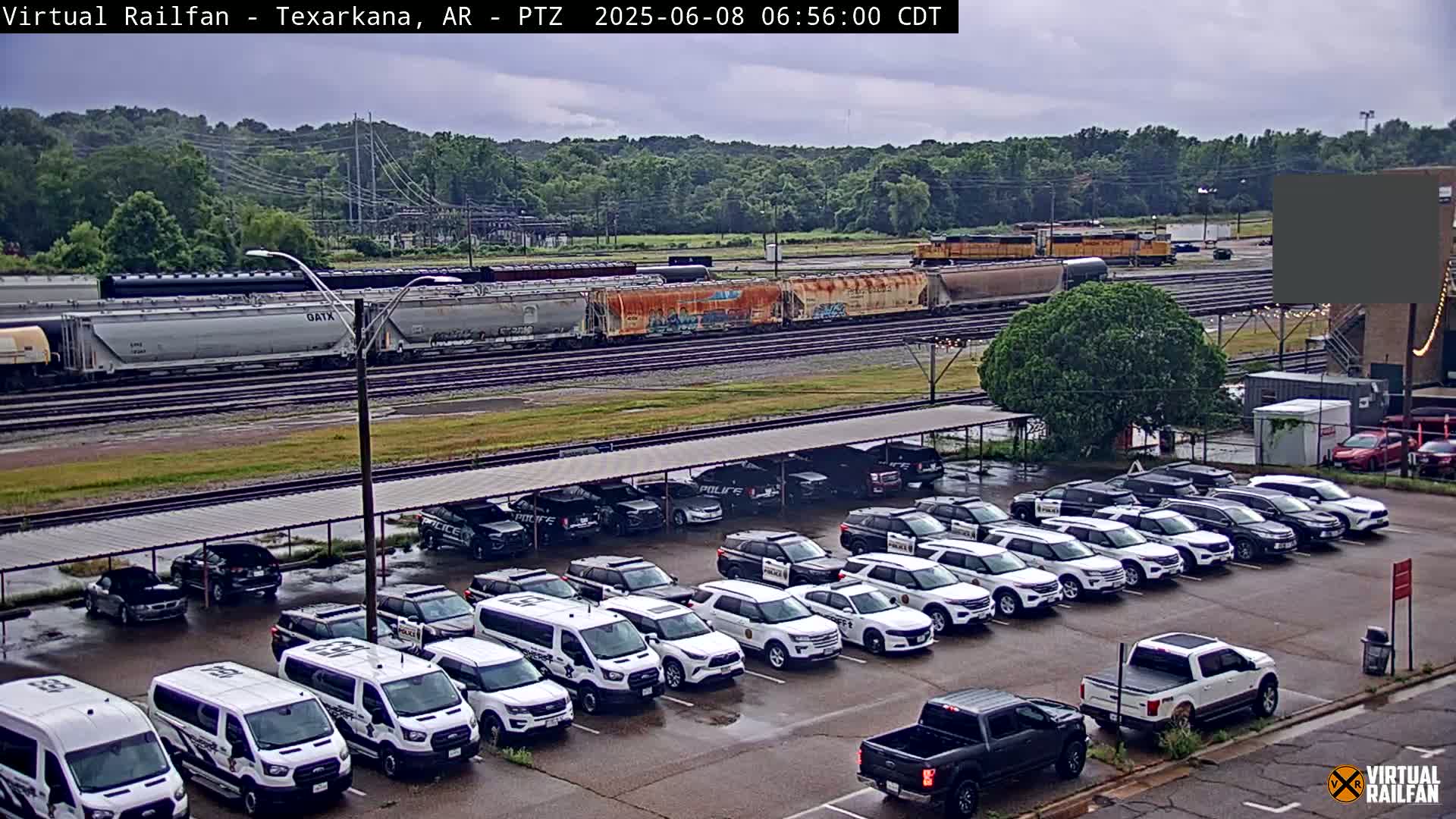 A freight train passes by a parking lot full of police vehicles under an overcast sky.