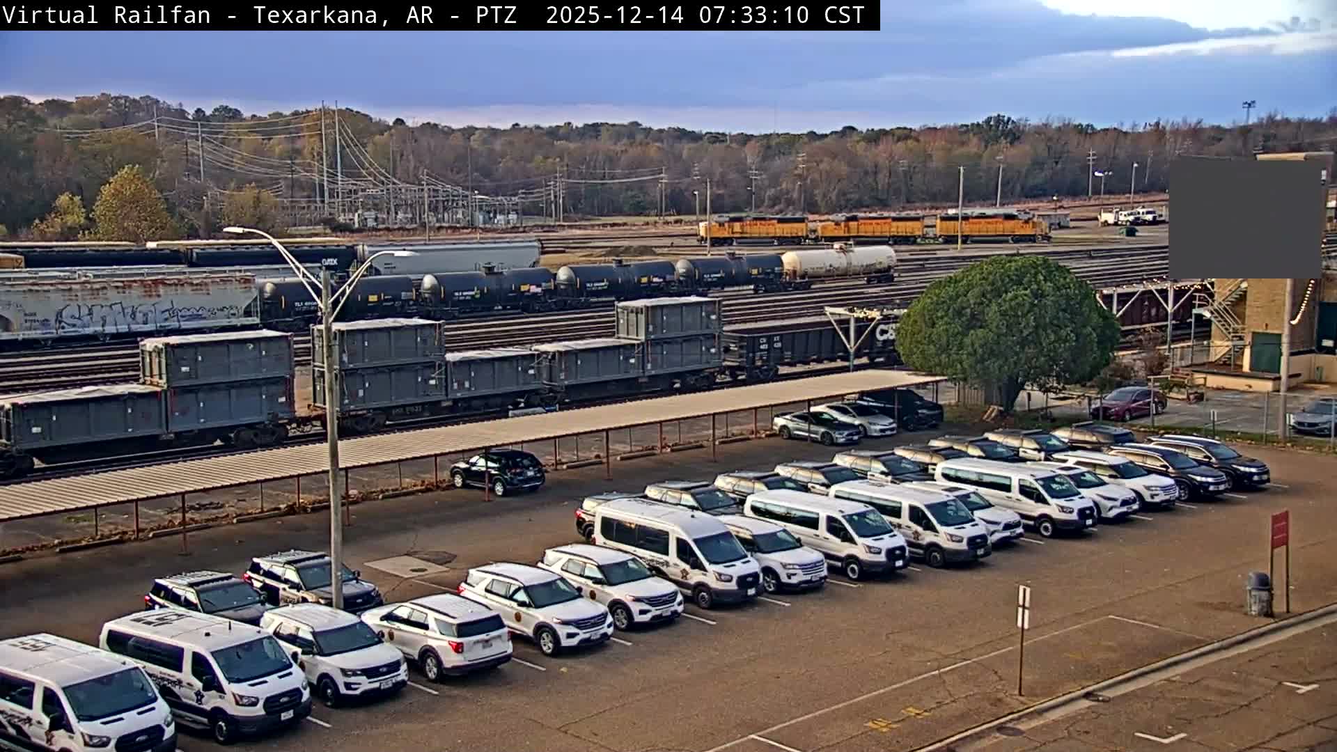 The image depicts a brightly lit outdoor parking lot at night with clear skies, filled with a mix of white vans and black and white SUVs (many resembling police vehicles), bordered by active train tracks with visible freight cars in the distance.