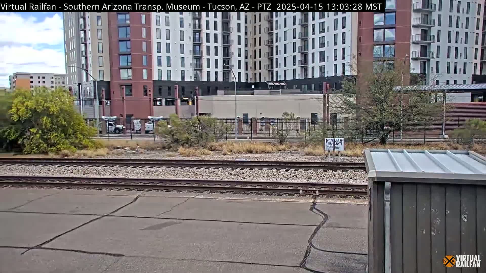 A view of railroad tracks next to a multi-story building under a partly cloudy sky.