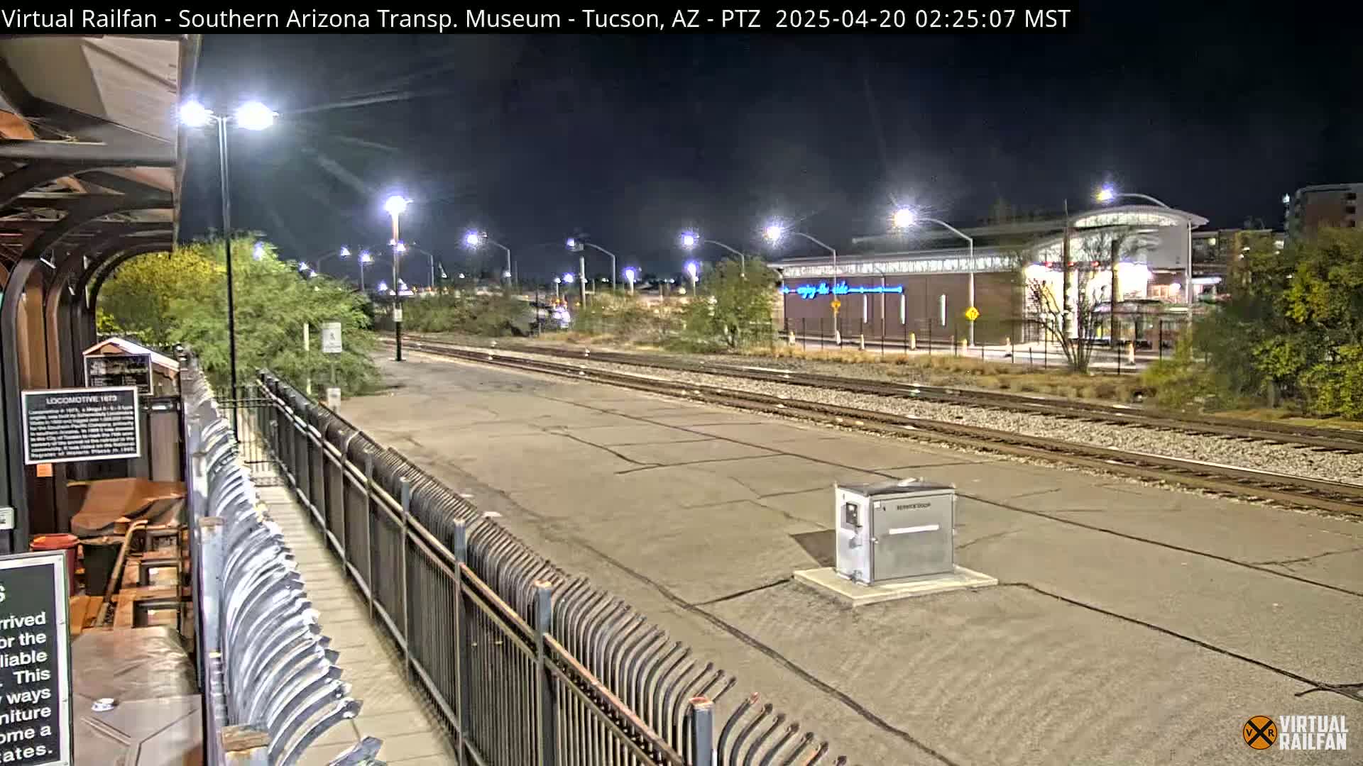 A nighttime view of train tracks and a station platform, illuminated by streetlights.