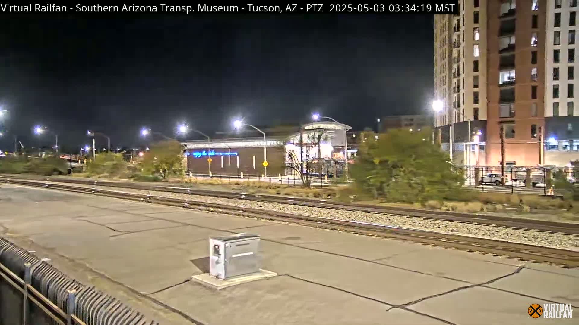A nighttime view of train tracks and a station platform next to a tall building, under clear skies.