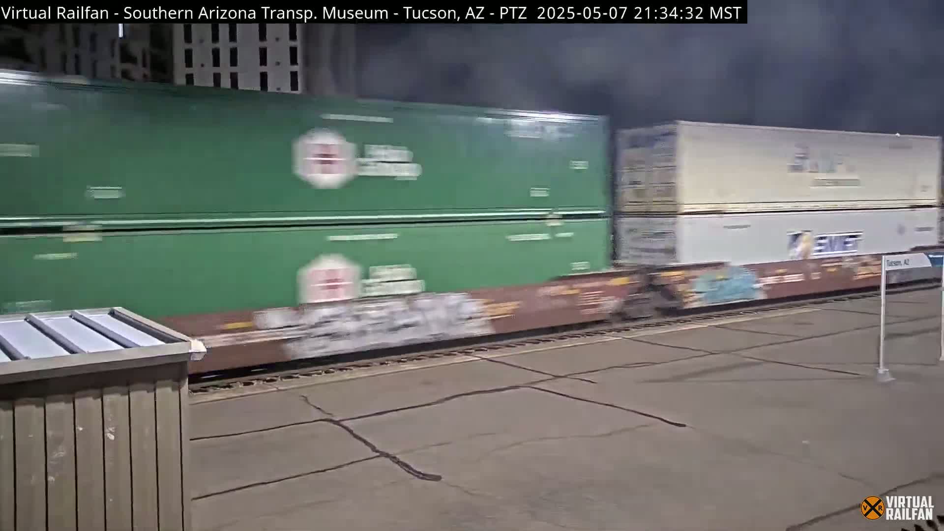 A freight train with green and beige containers passes by at night.