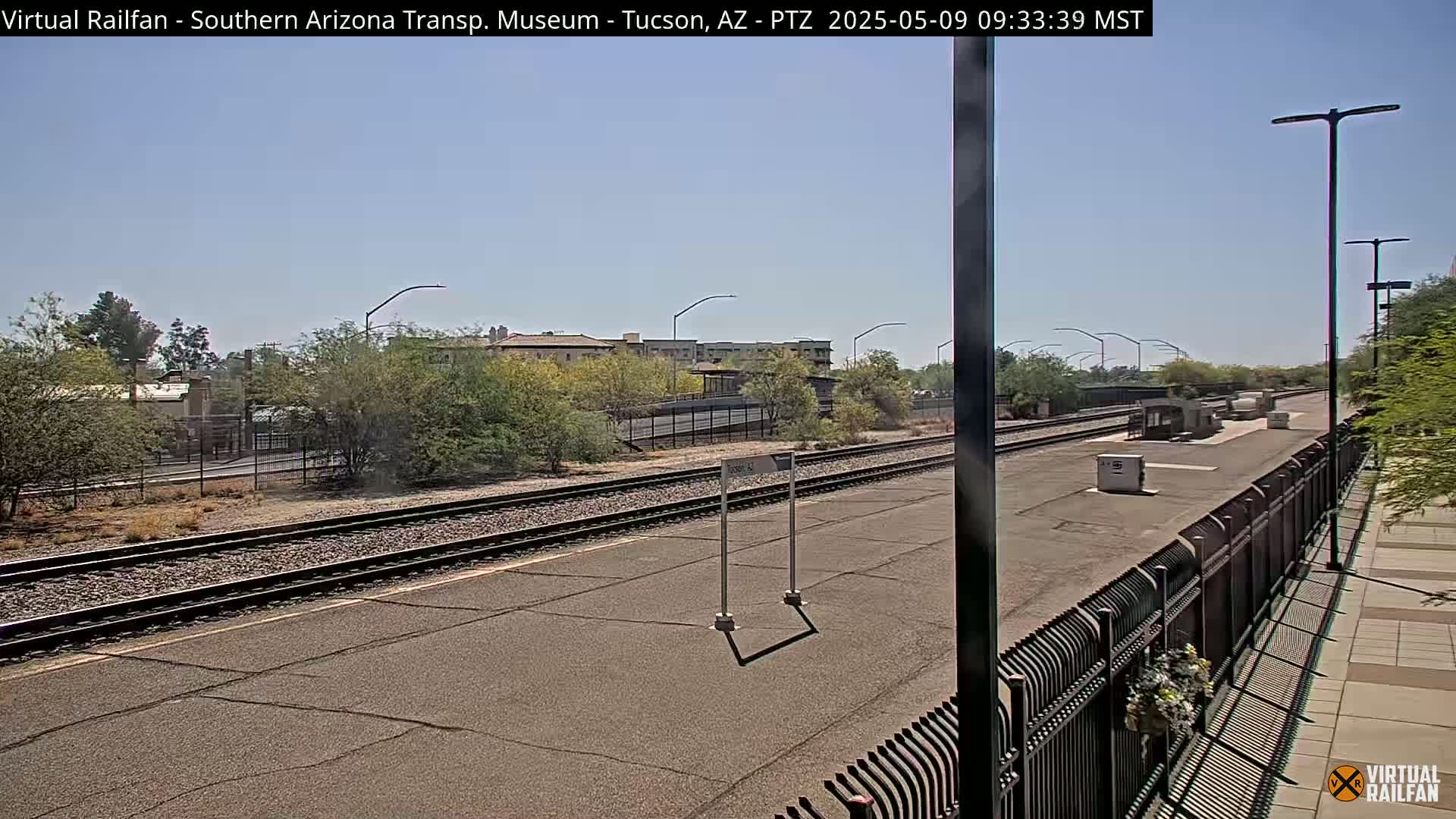 A train station platform with several tracks and a clear, sunny sky.