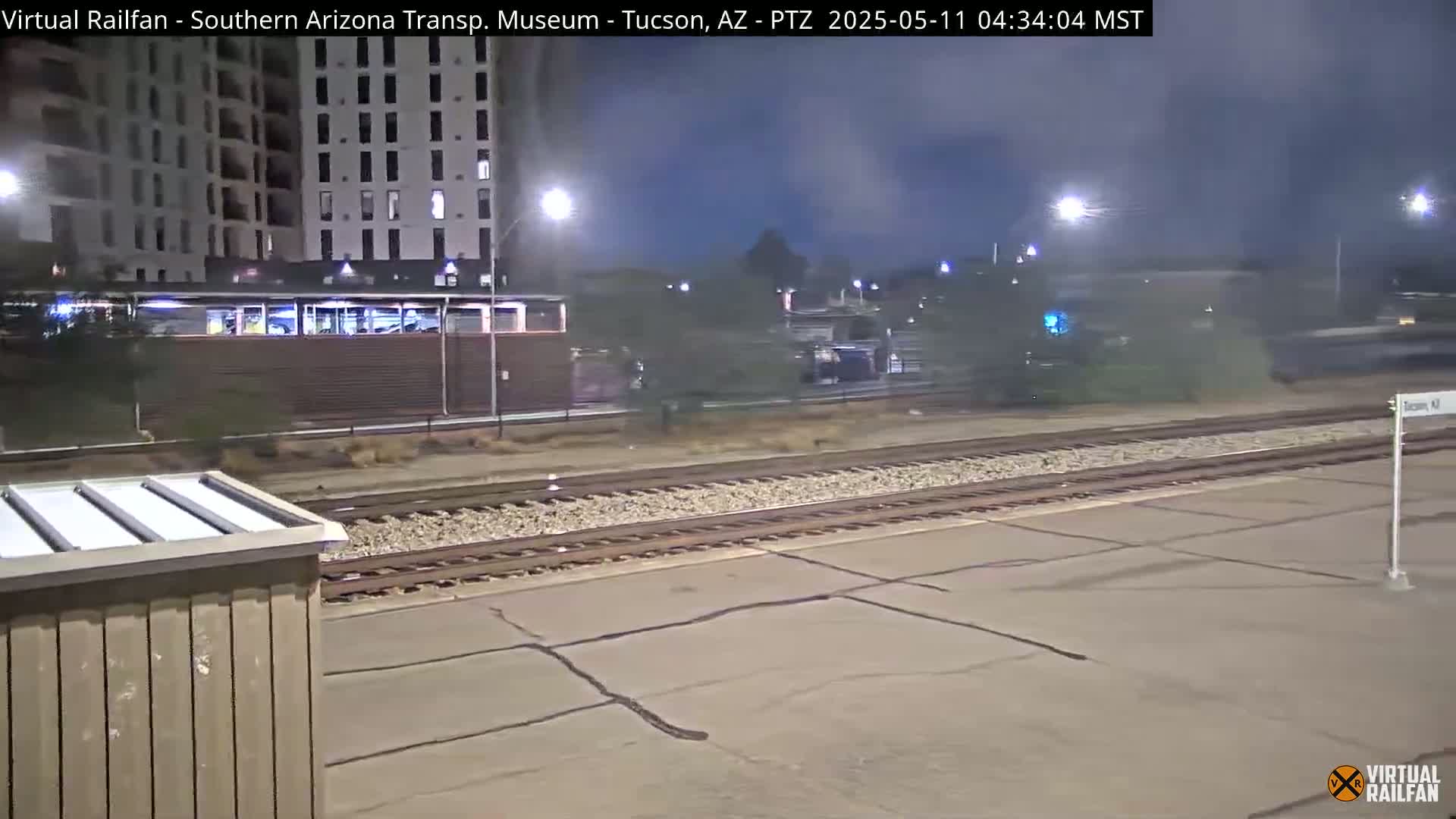 A nighttime view of railroad tracks near a building, with a train in the distance under hazy conditions.