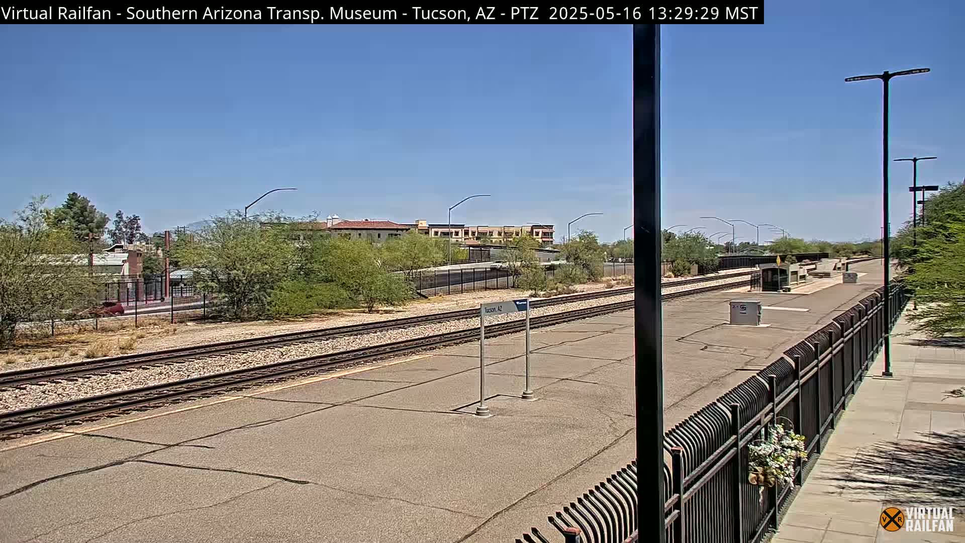 A train station platform with railroad tracks and a clear blue sky.