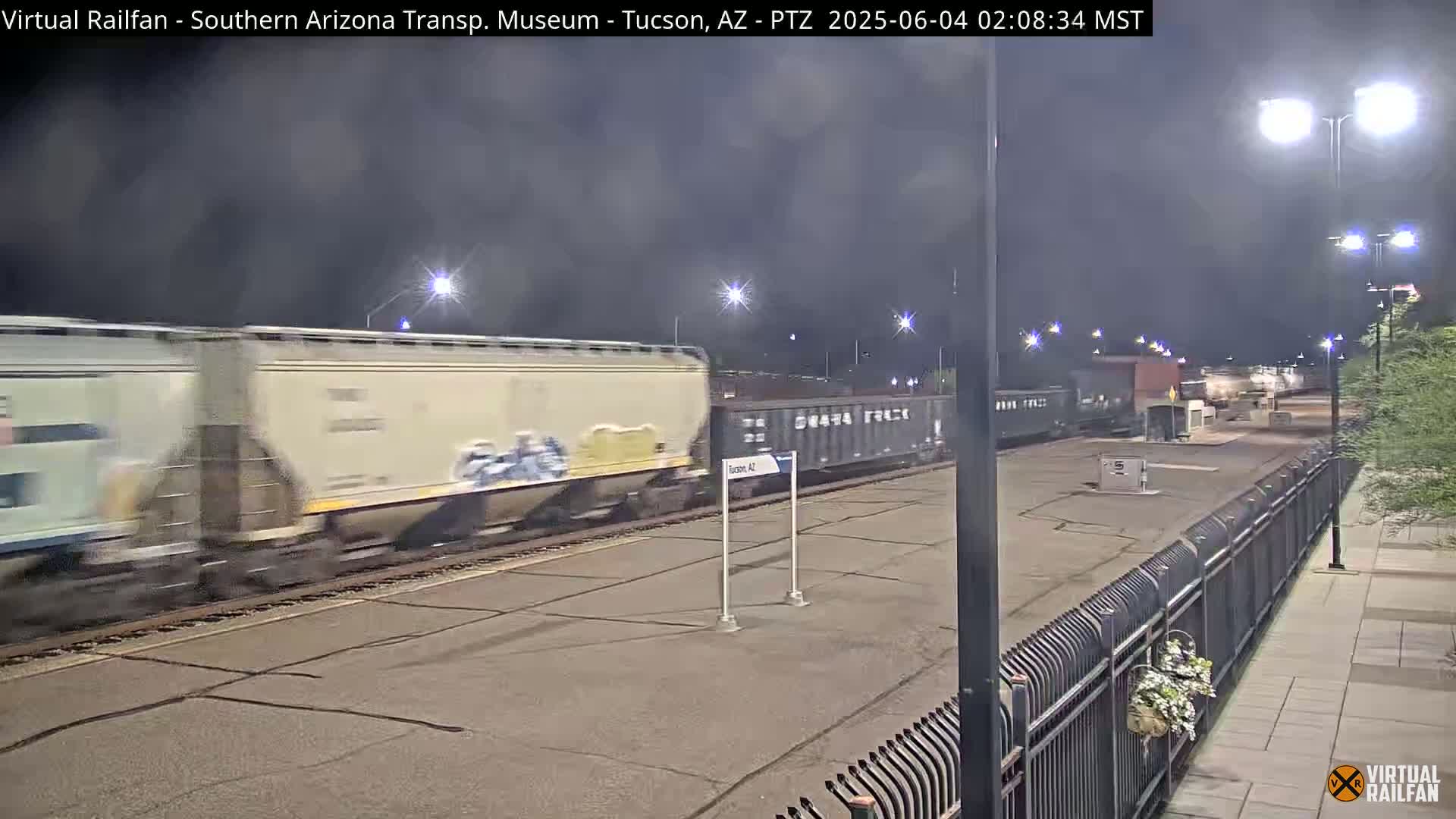 A freight train passes by at night under partly cloudy skies.