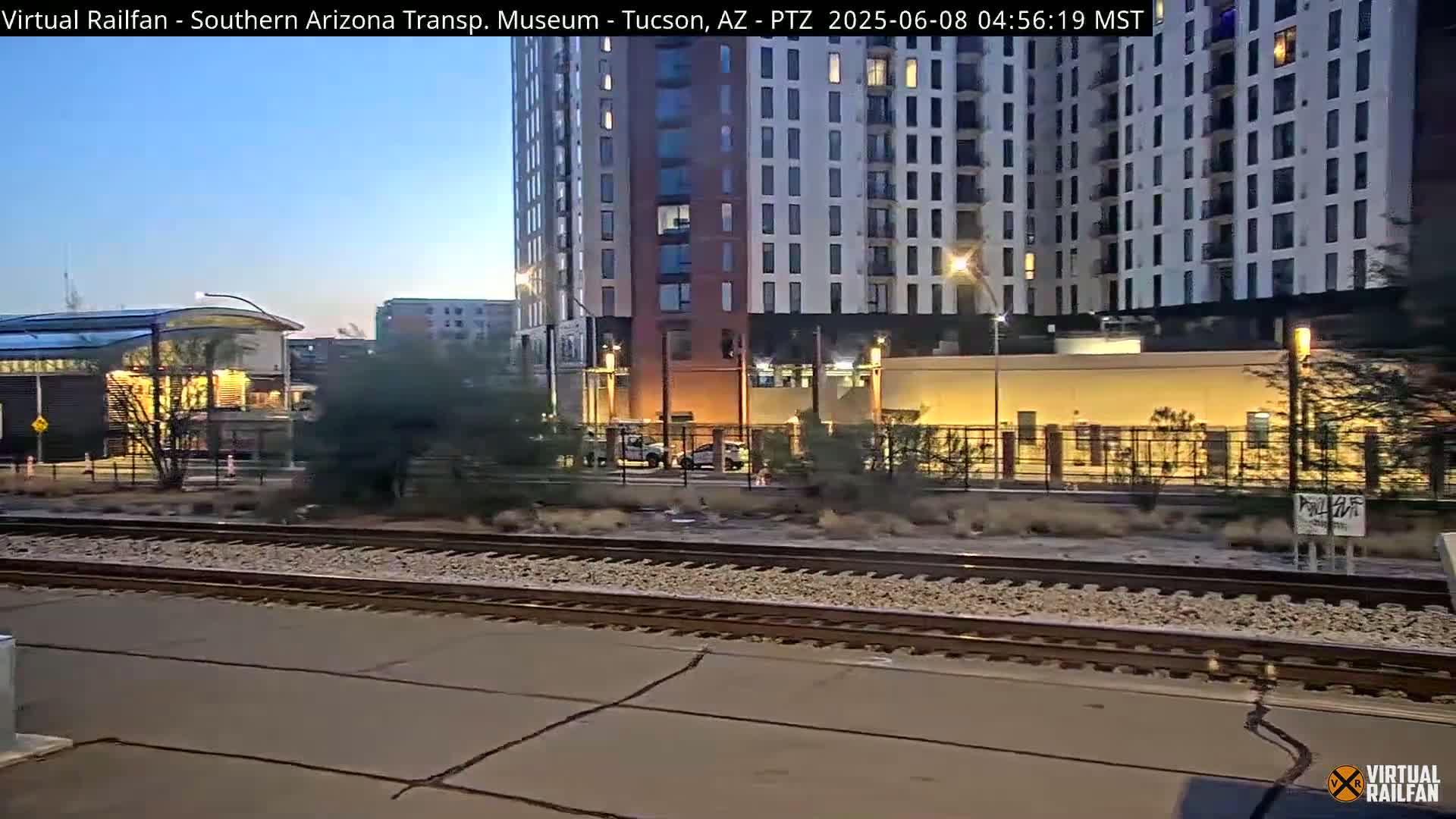A train track runs in front of a modern building complex at dusk.
