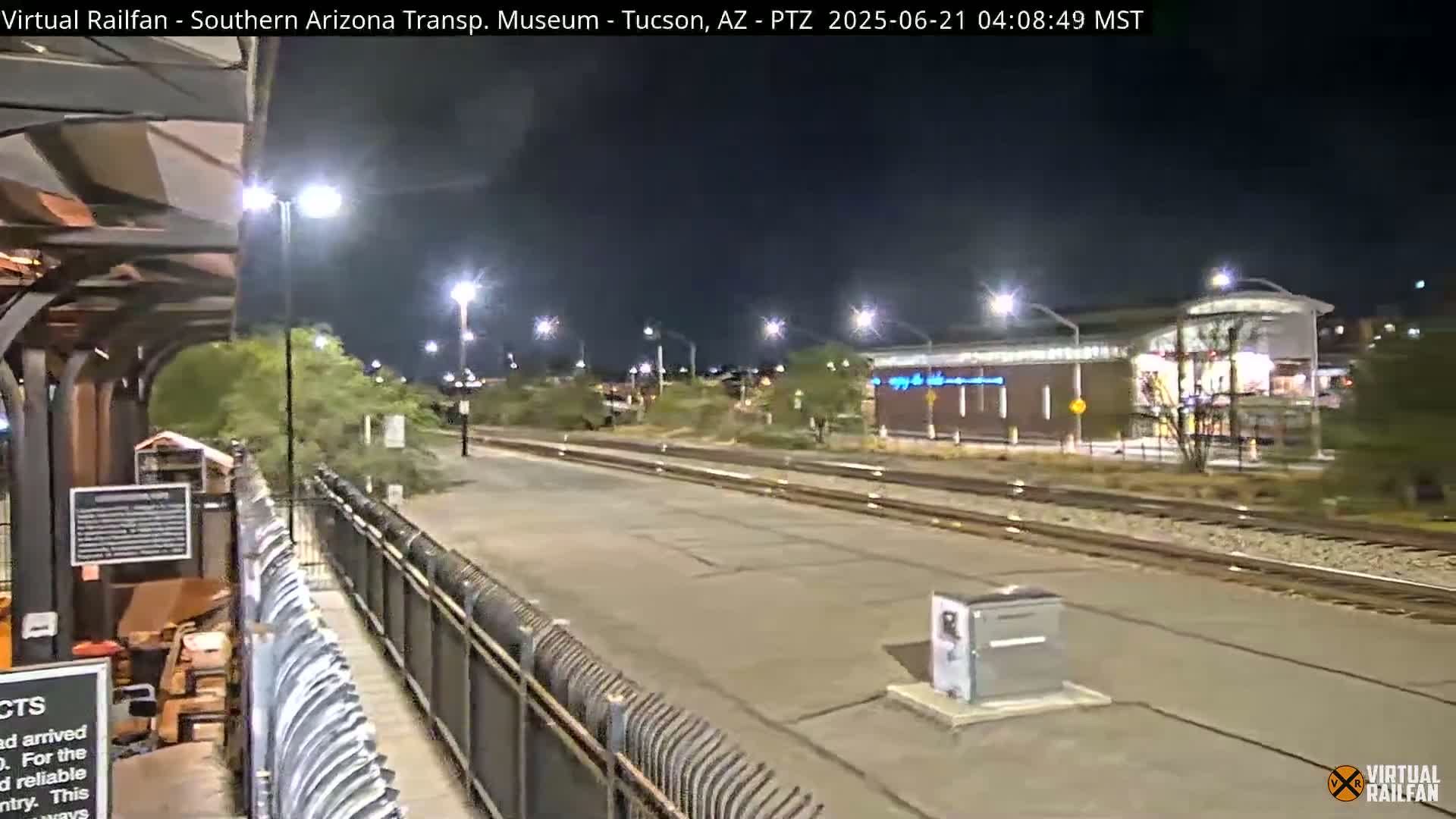 A nighttime view of a train station platform with tracks extending into the distance under artificial lighting.