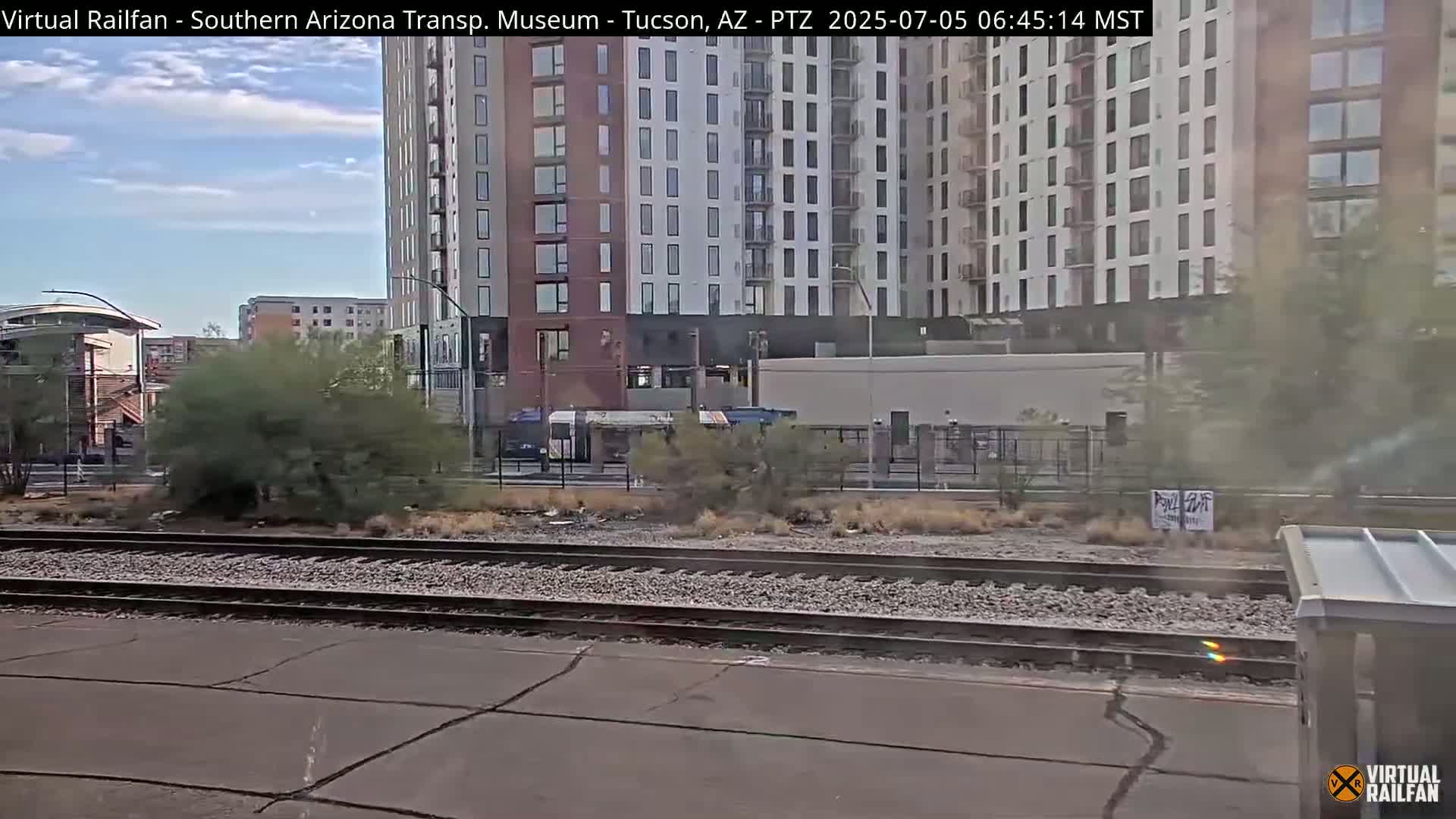 A view of railroad tracks in front of a multi-story apartment building on a partly cloudy day.