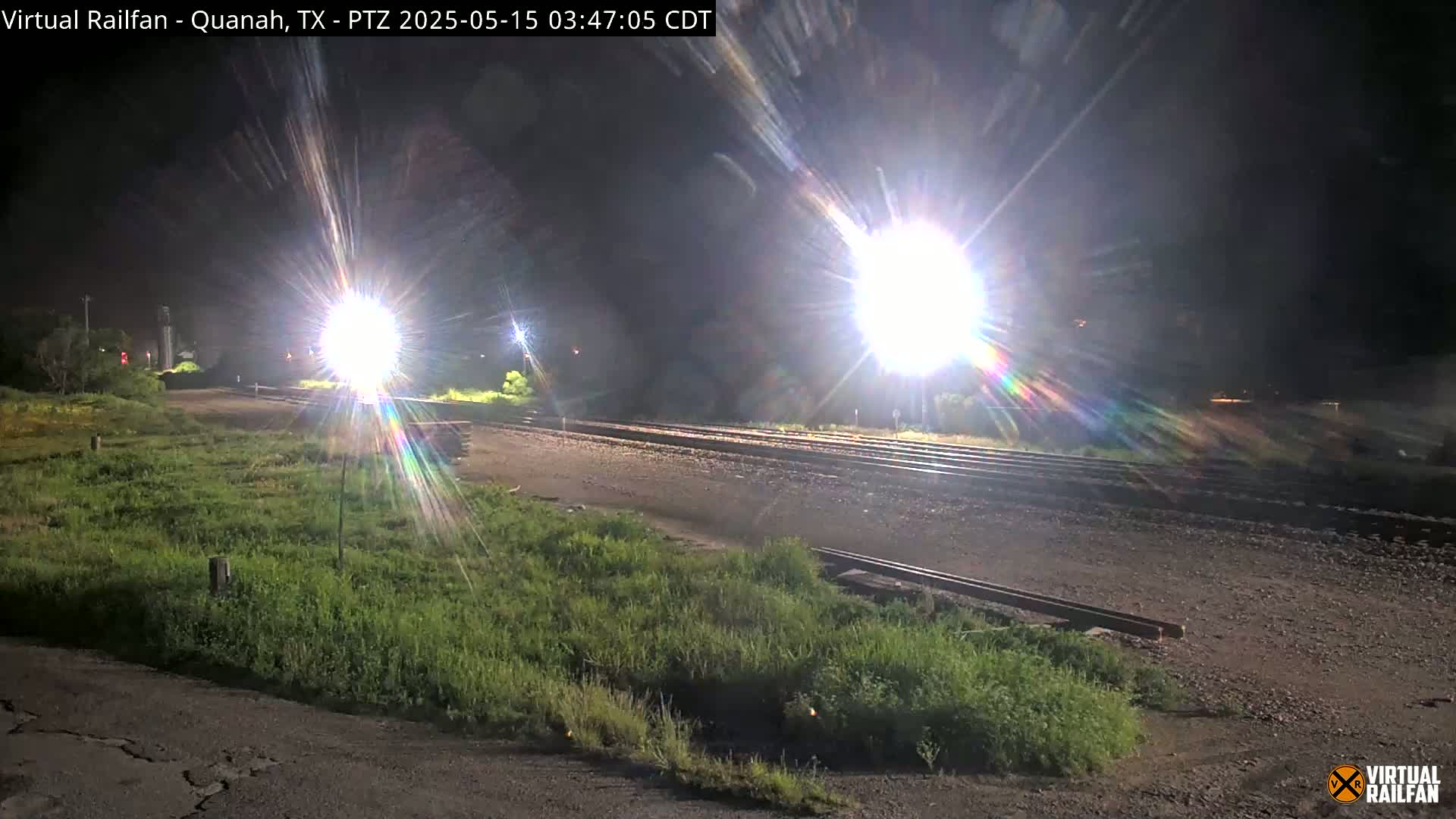 Brightly lit railroad tracks at night are surrounded by grassy areas.