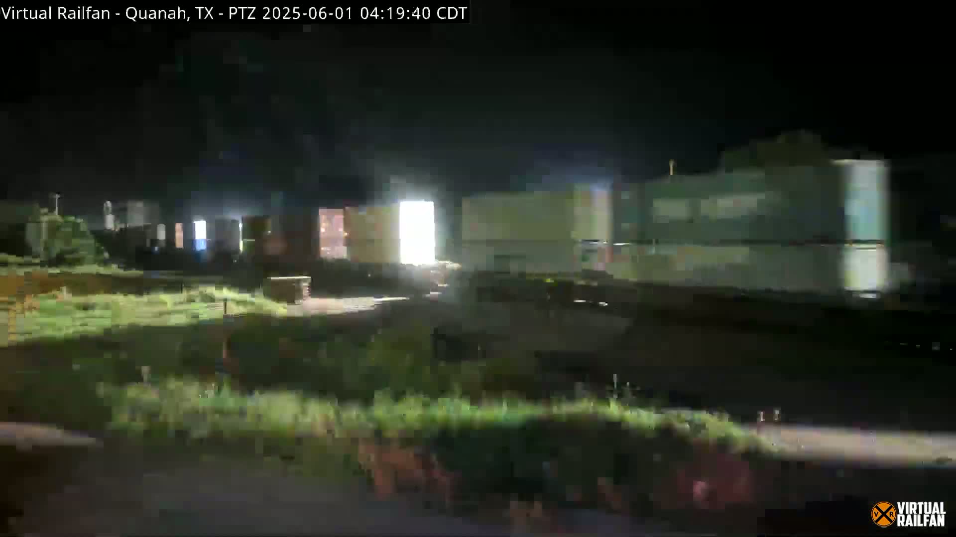 A long freight train moves through a dimly lit area at night.