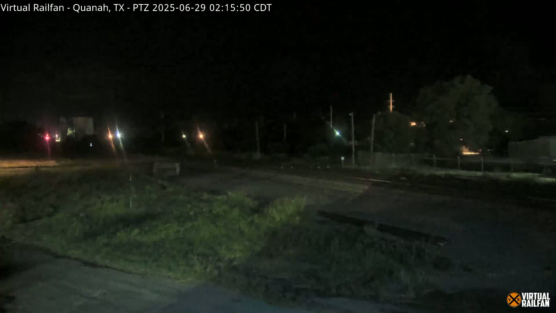 A nighttime view of a mostly empty field next to a road with some distant lights and vegetation.