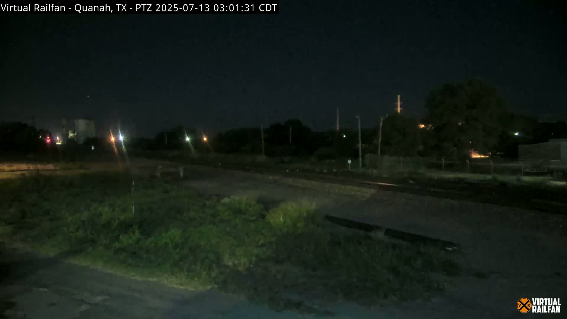 A nighttime view of a railroad track bordered by vegetation under a clear, dark sky.