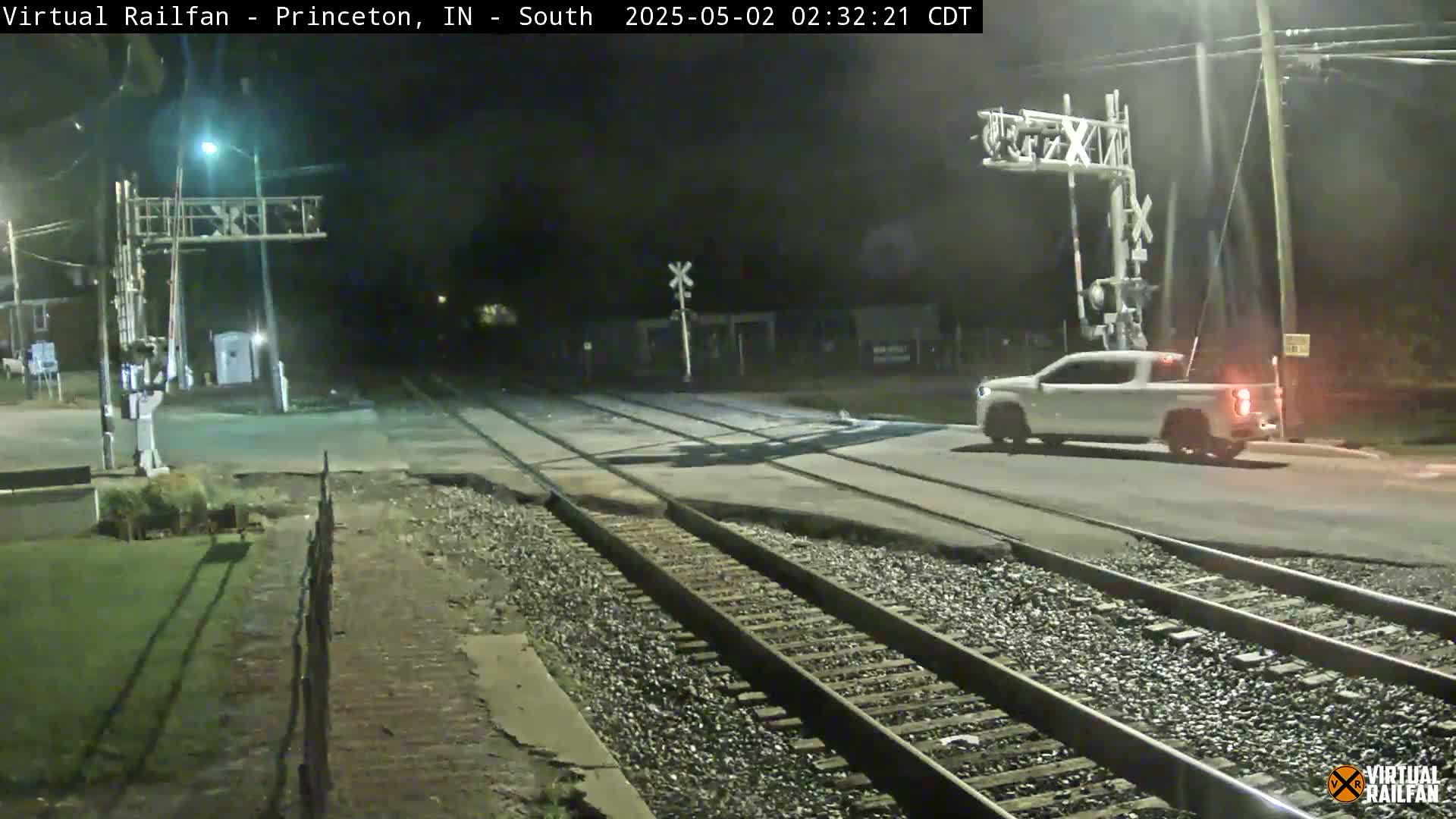 A white pickup truck drives across a railroad crossing at night.