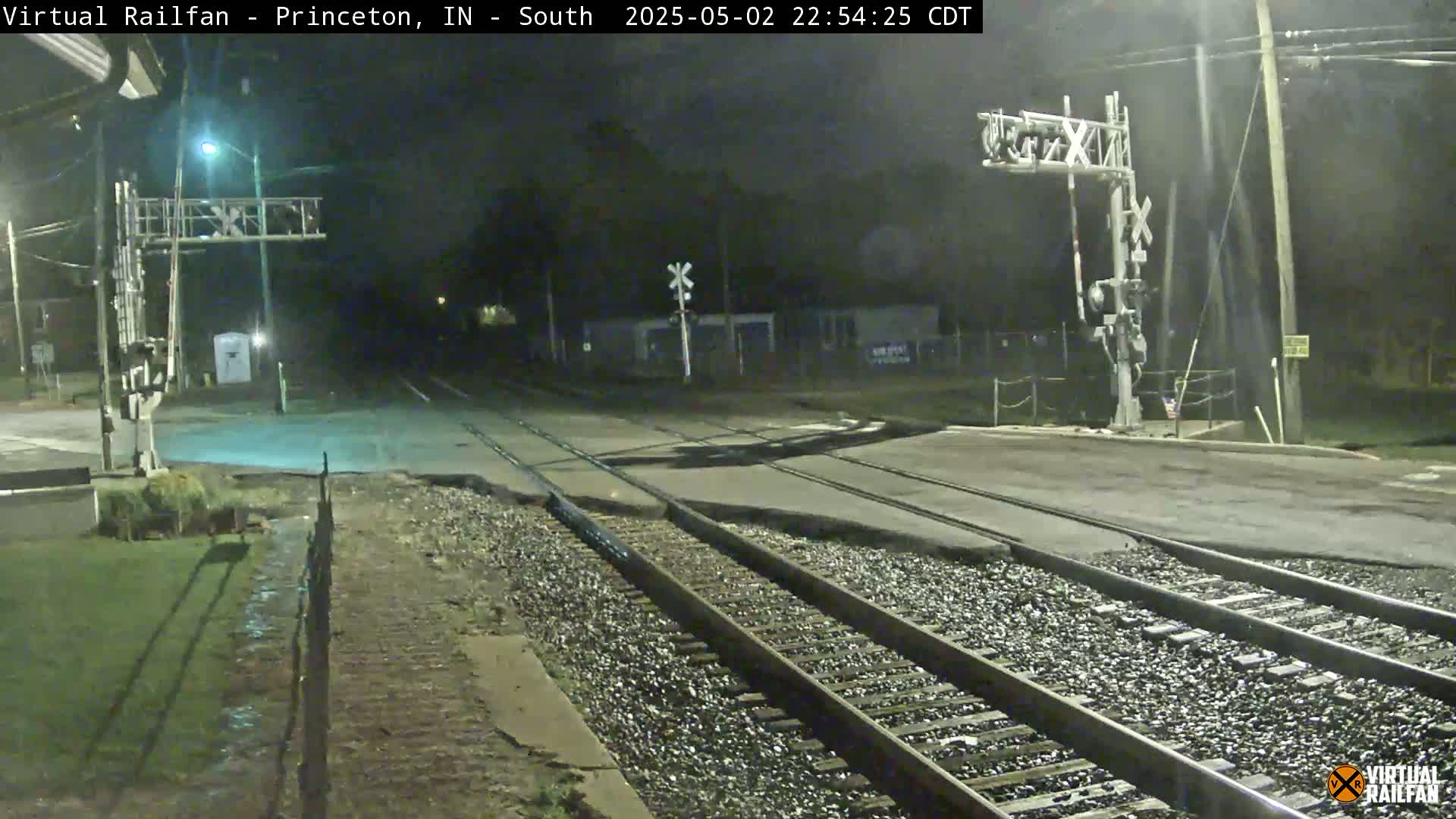 A nighttime view of a railroad crossing with train tracks intersecting a road under clear skies.
