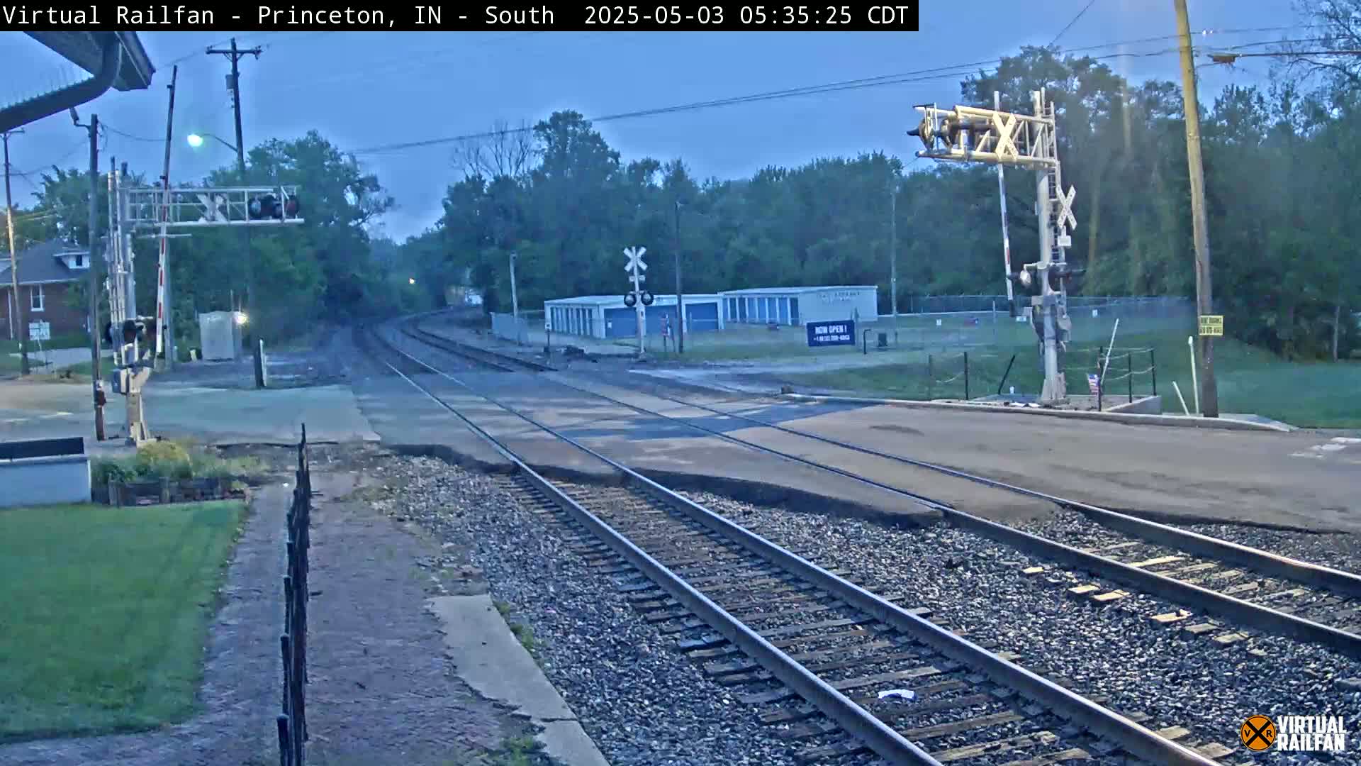 A nighttime view of a railroad crossing with train tracks intersecting a road, under a twilight sky.