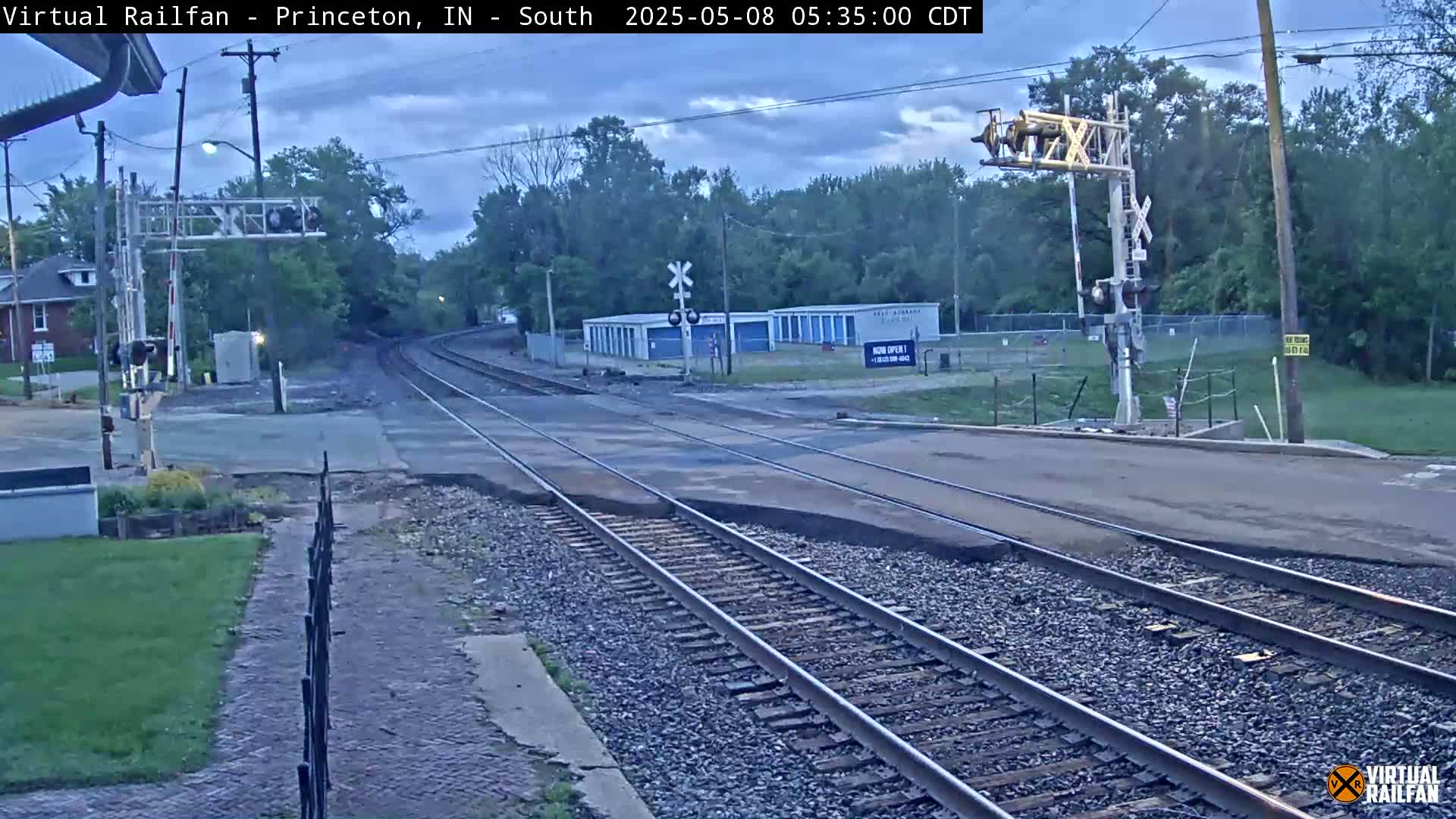 A railroad crossing with train tracks and a road intersecting under an overcast sky.