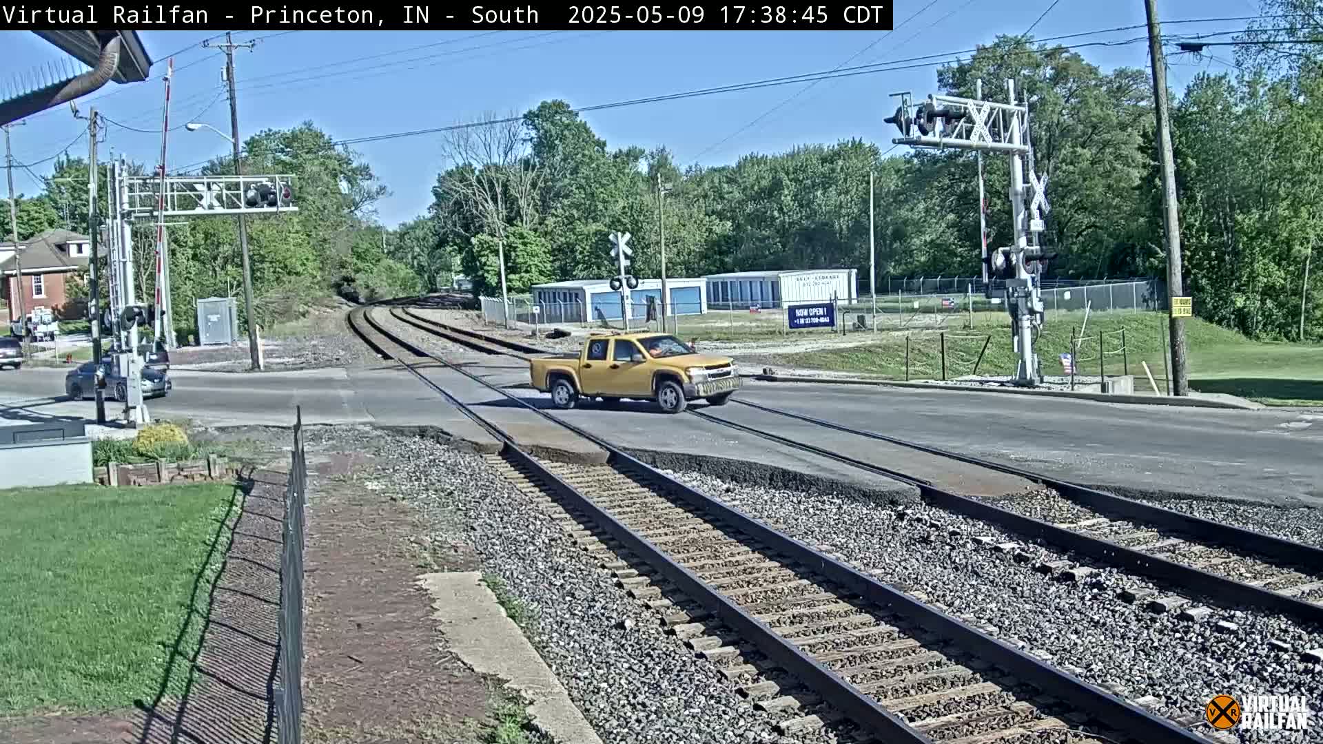 A yellow pickup truck is crossing a railroad intersection under a mostly sunny sky.