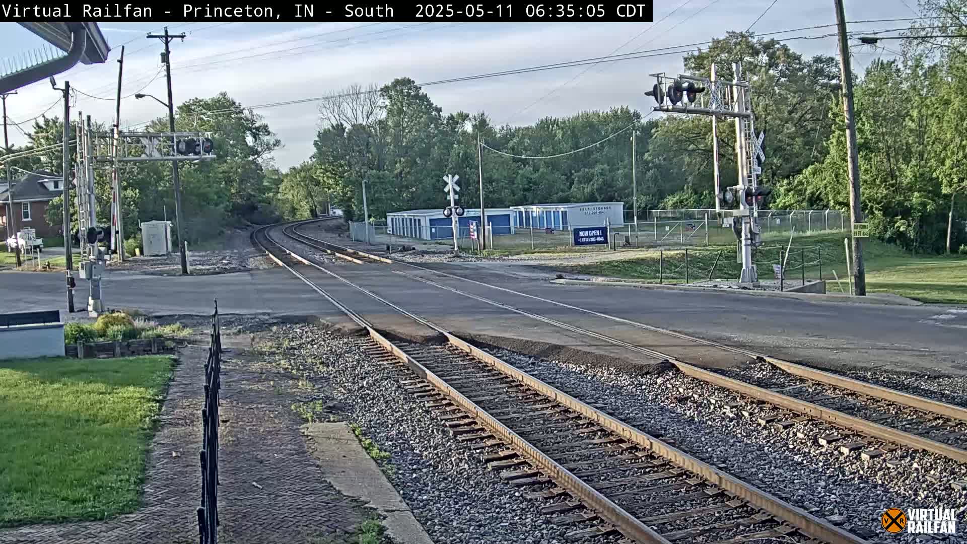 Railroad tracks cross a road in front of a row of storage units under a partly cloudy sky.