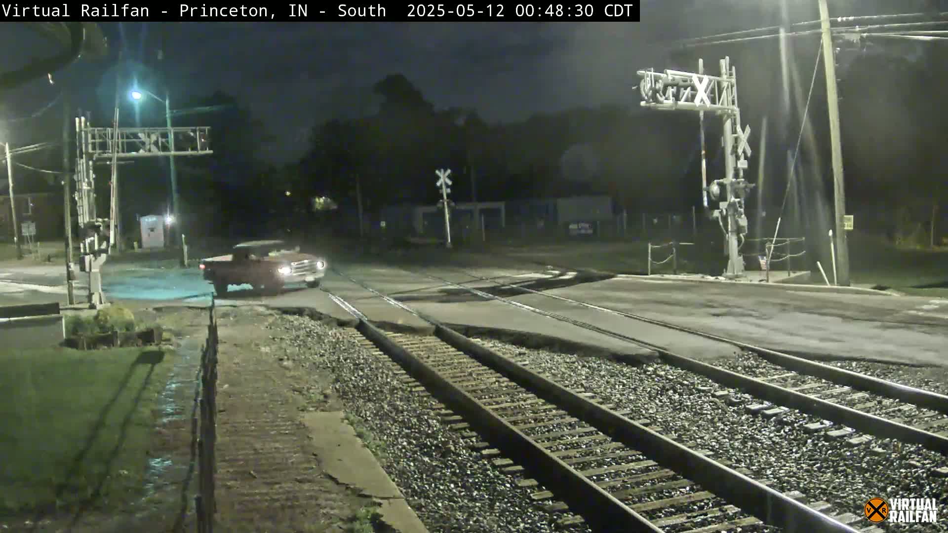 A red pickup truck drives across a railroad crossing at night, under mostly clear skies.