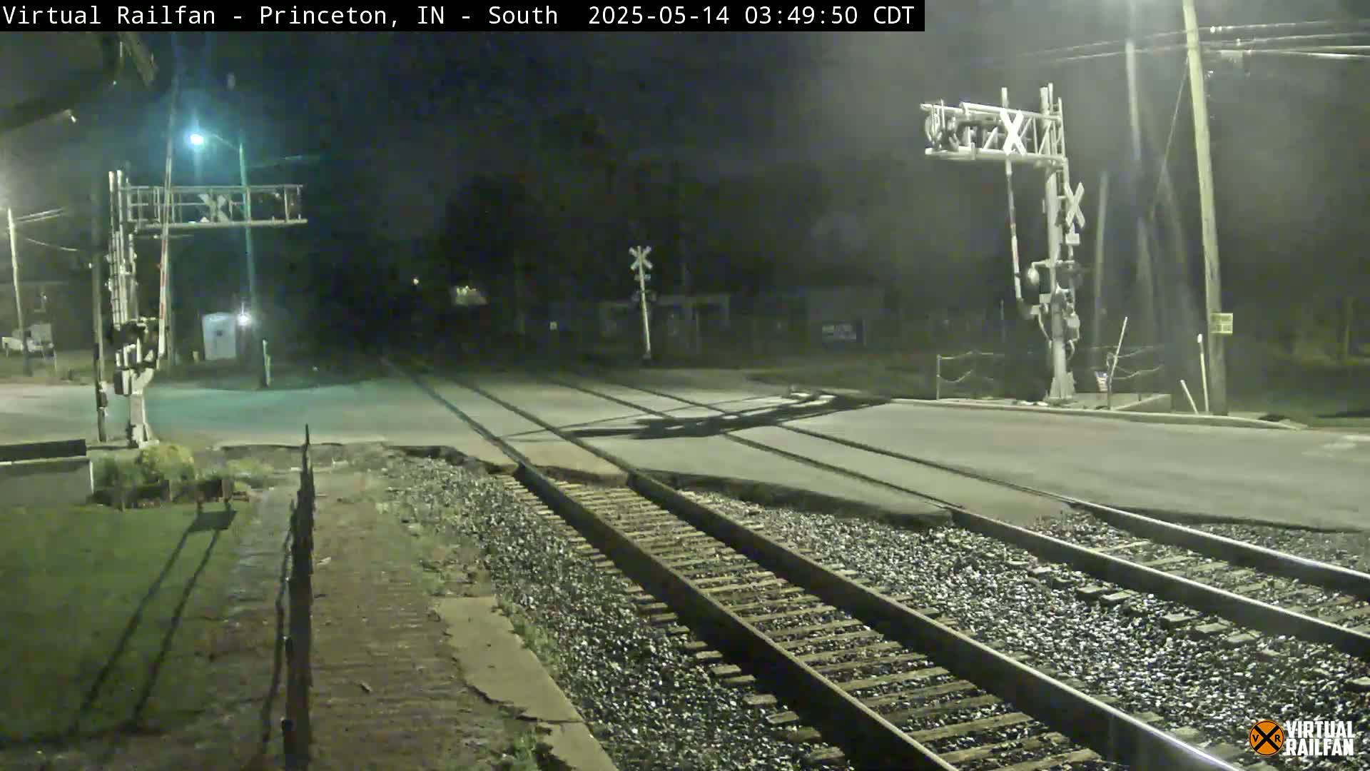 A nighttime view of a railroad crossing with train tracks and crossing signals under clear skies.