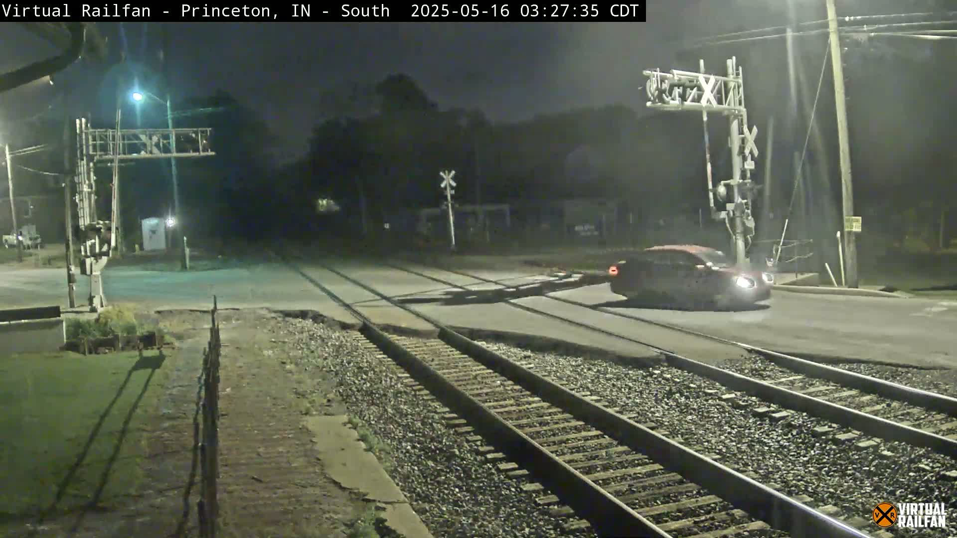 A car drives across a railroad crossing at night under dark, overcast skies.