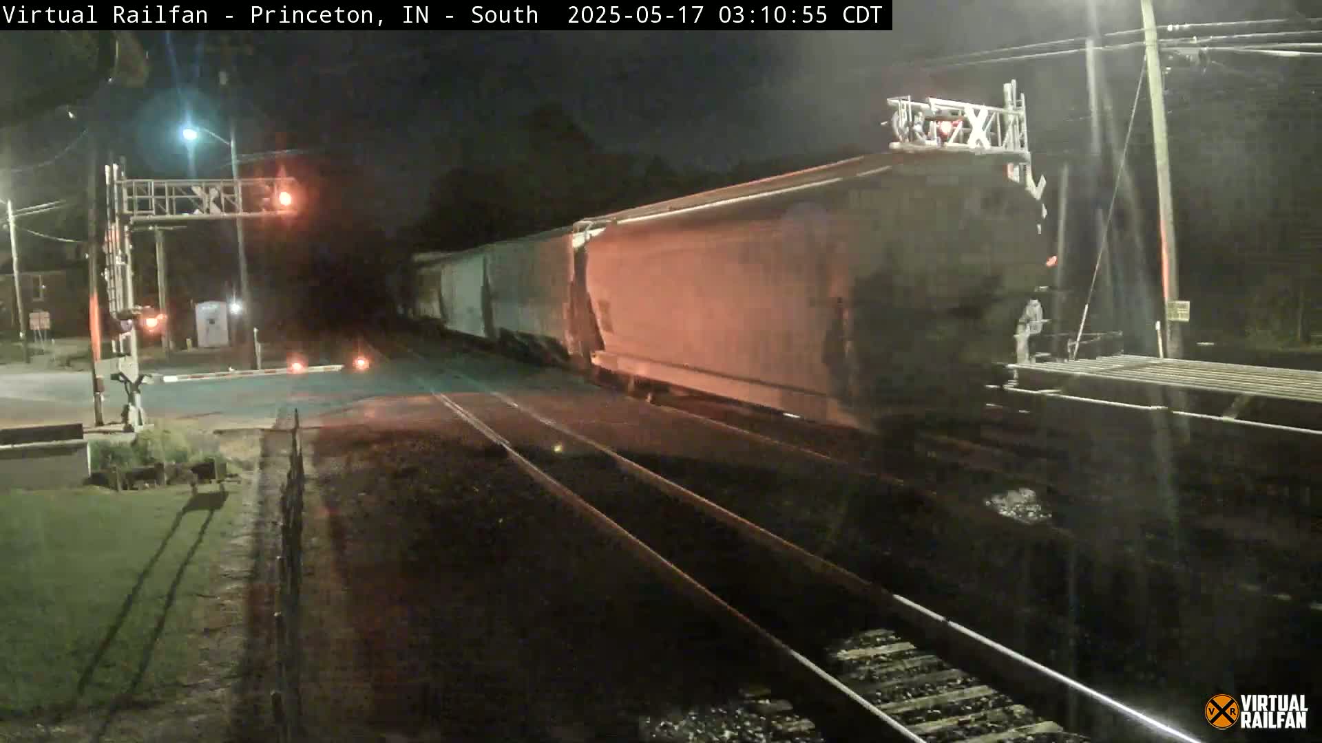 A long freight train passes a railroad crossing at night under dark, clear skies.