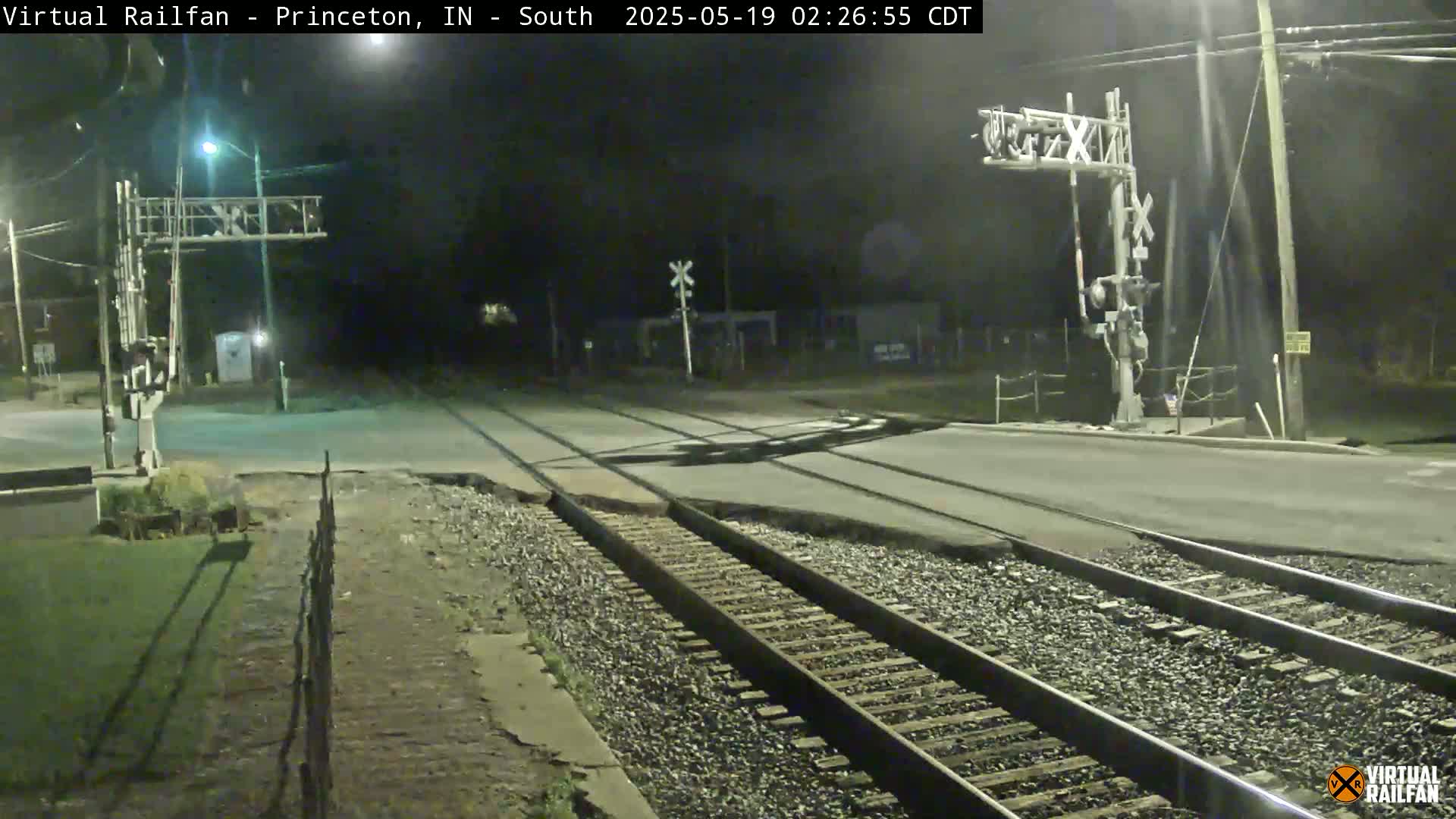 A nighttime view of a railroad crossing with two sets of tracks intersecting a road under dark, clear skies.