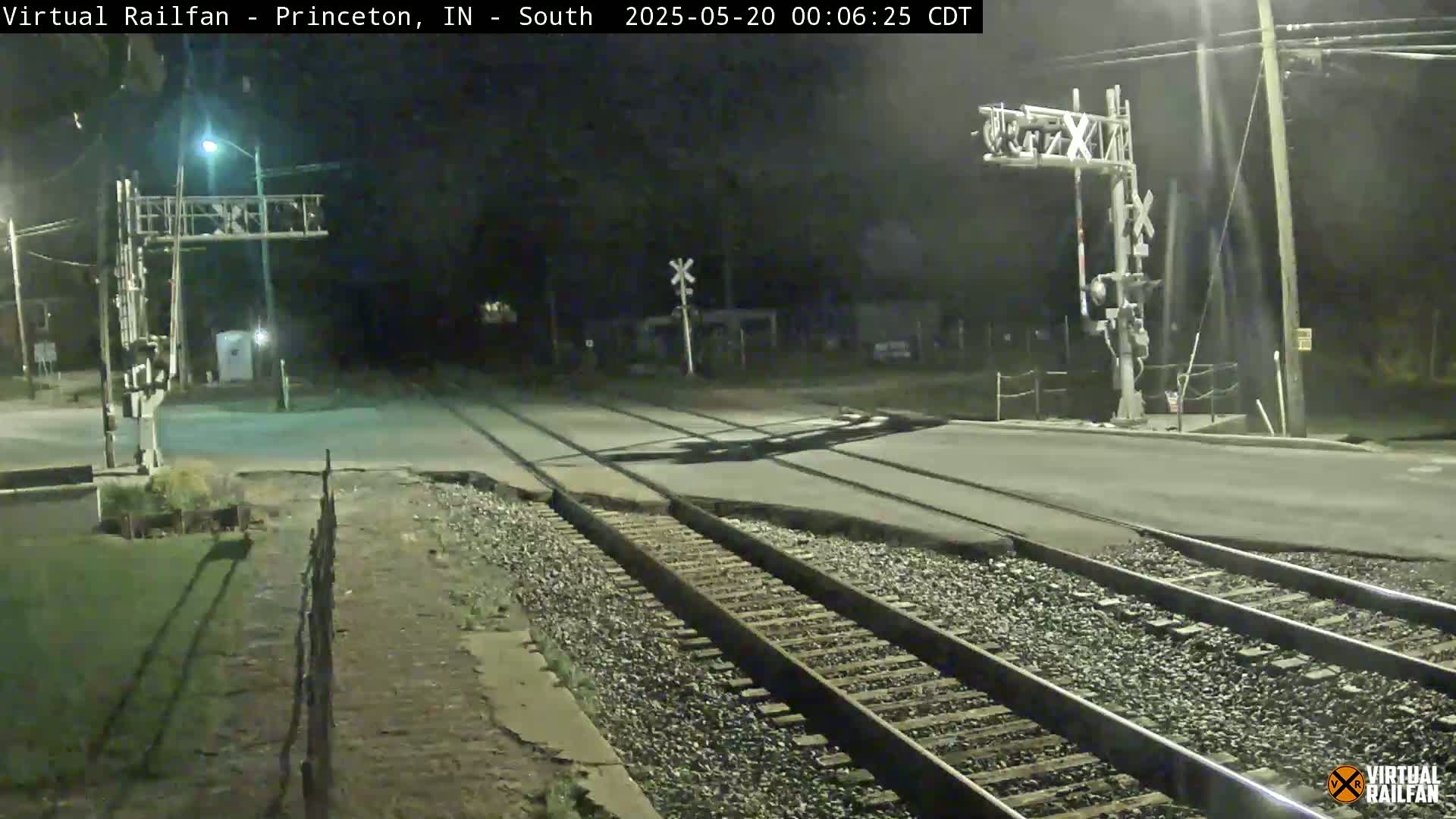 A nighttime view of a railroad crossing with a road intersecting the tracks, illuminated by streetlights.