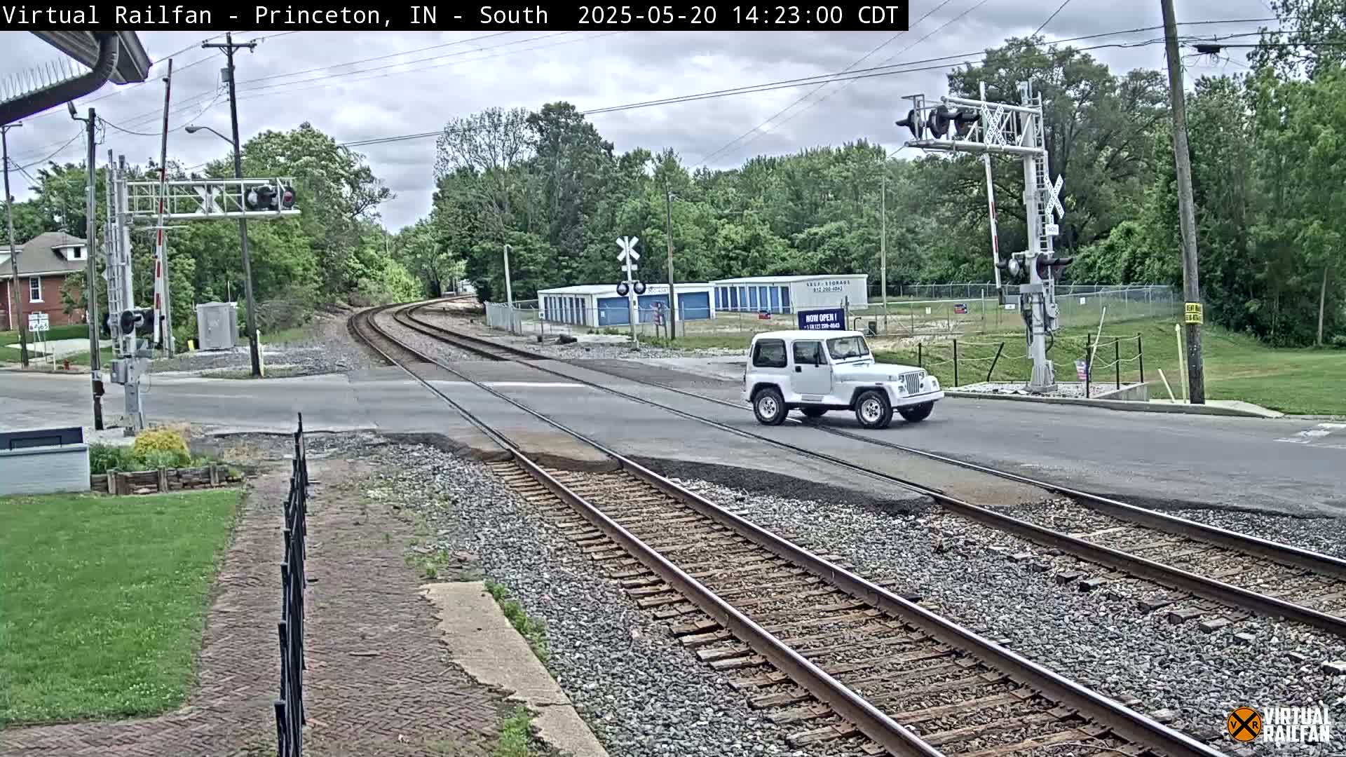 A white Jeep drives across a road intersecting railroad tracks under a partly cloudy sky.