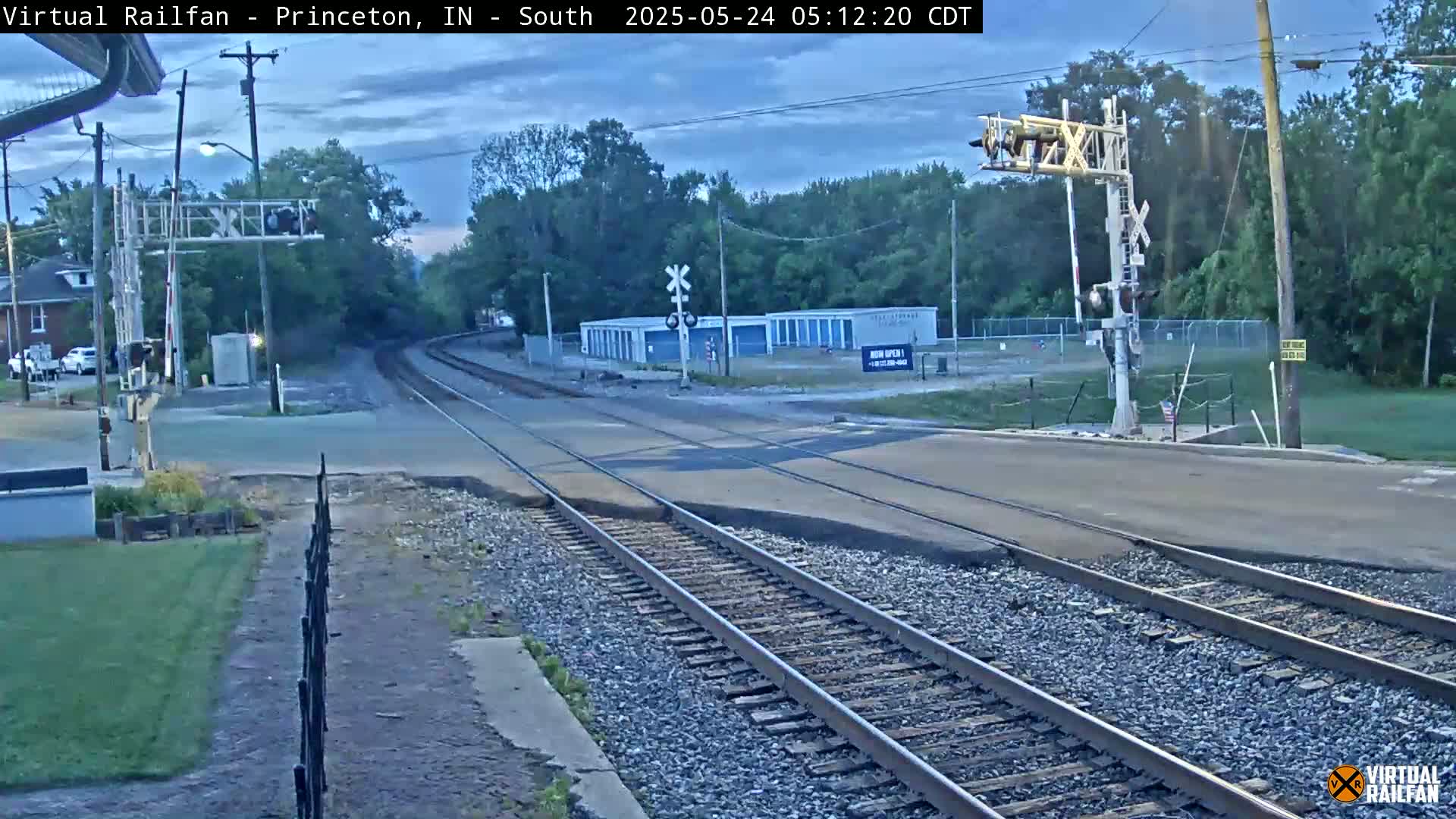 A railroad crossing with train tracks and a road intersecting under a twilight sky.