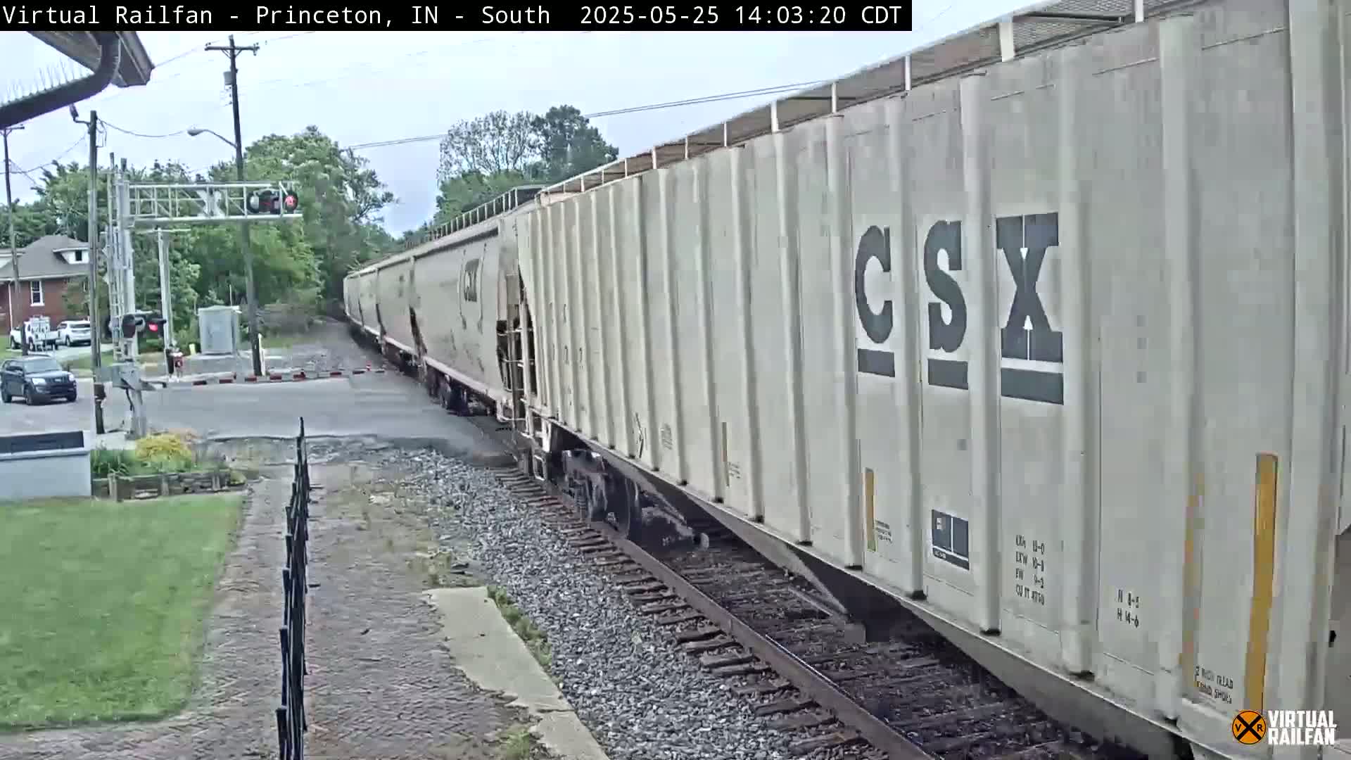A long CSX freight train passes a road crossing on a partly cloudy day.