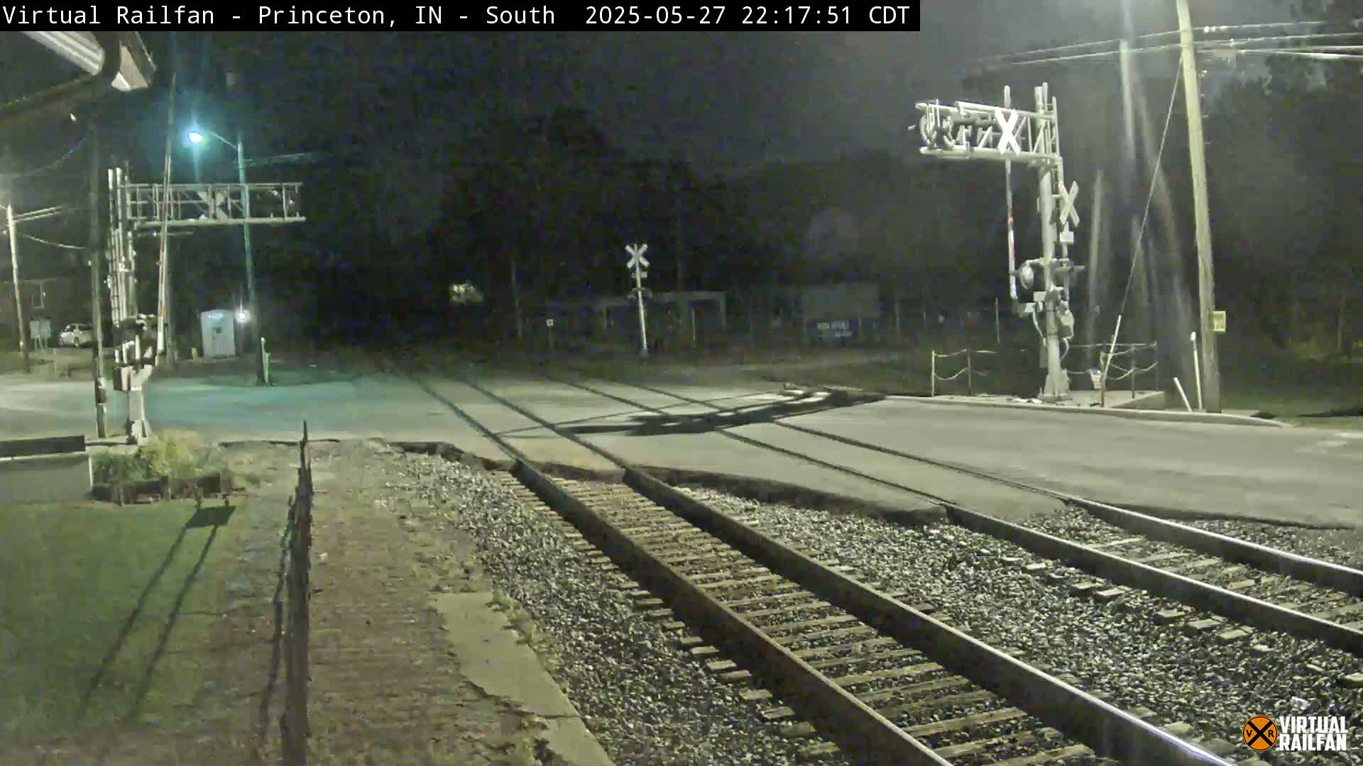 A nighttime view of a railroad crossing with train tracks intersecting a road under illuminated crossing signals.