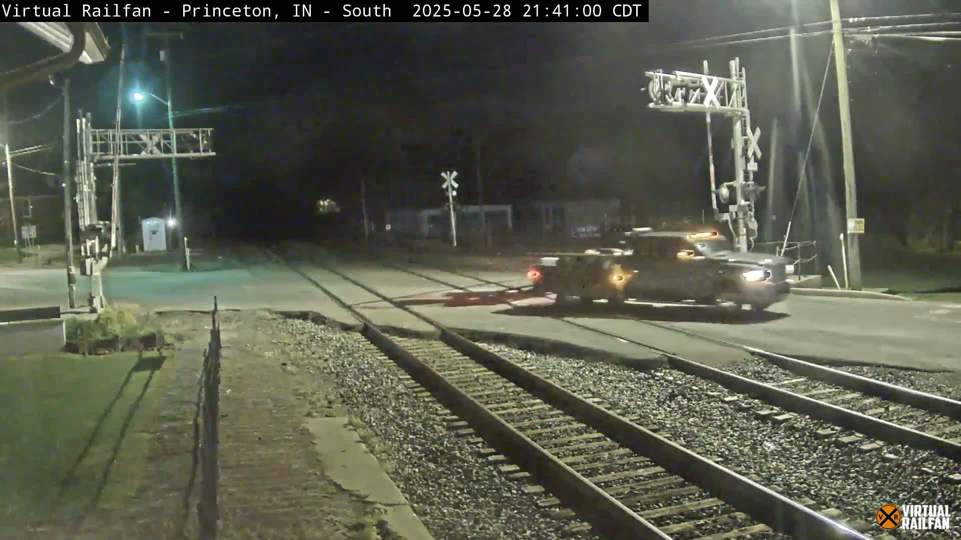 A dark-colored truck is crossing a railroad crossing at night under a dark sky.