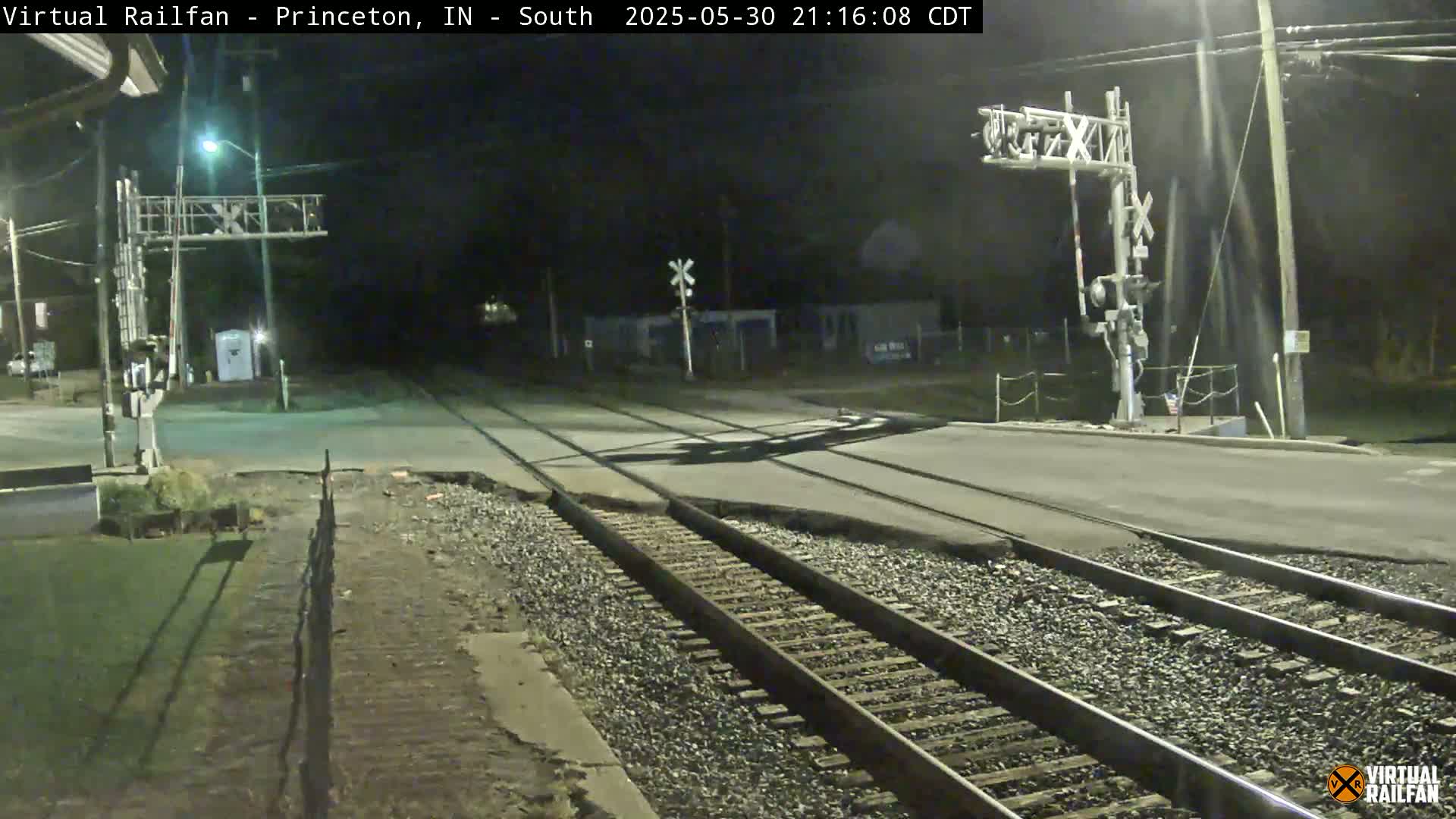 A nighttime view of a railroad crossing with a road intersecting the tracks under the illuminated railroad crossing signal.