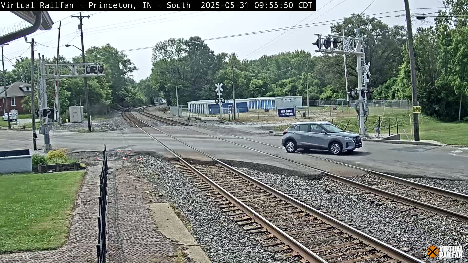 A silver SUV drives across a road intersecting a railroad track under a mostly cloudy sky.