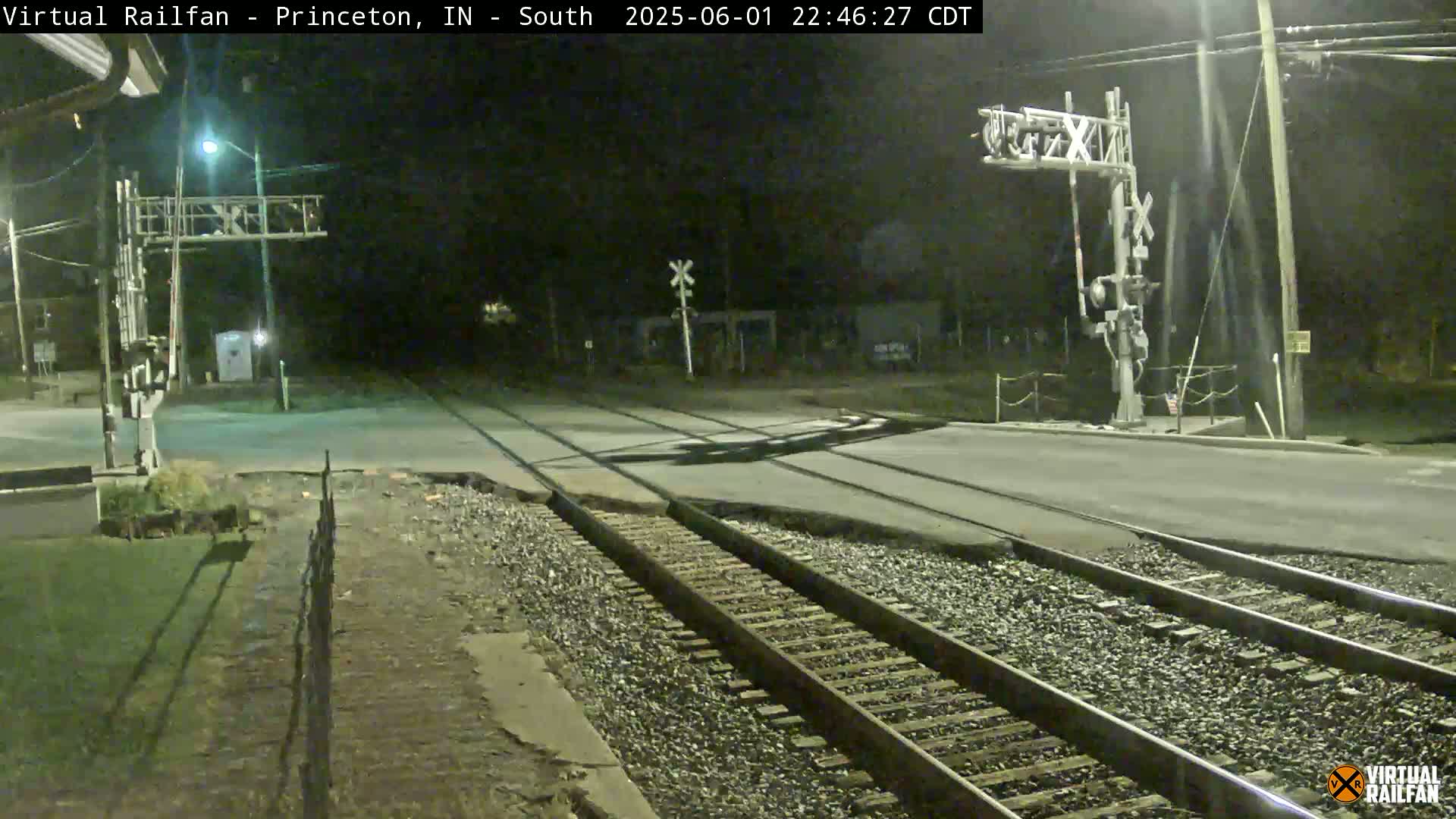 A nighttime view of a railroad crossing with a road intersecting the tracks, under clear skies.