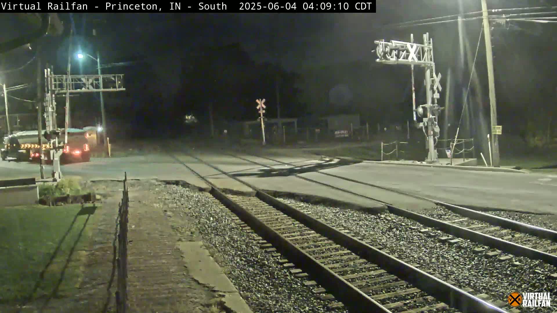 A nighttime view of a railroad crossing with a truck stopped near a railroad crossing gate, under dark conditions.