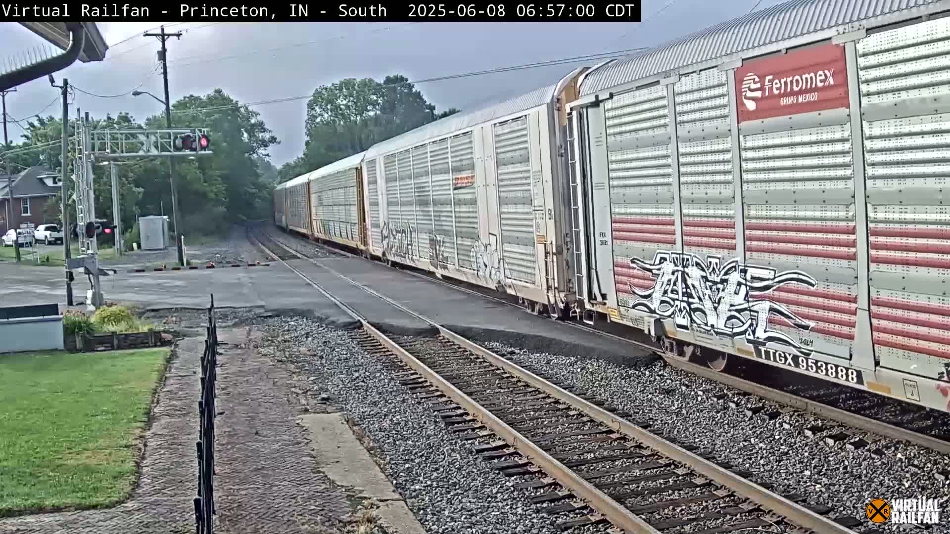 A long freight train passes a road crossing under an overcast sky.