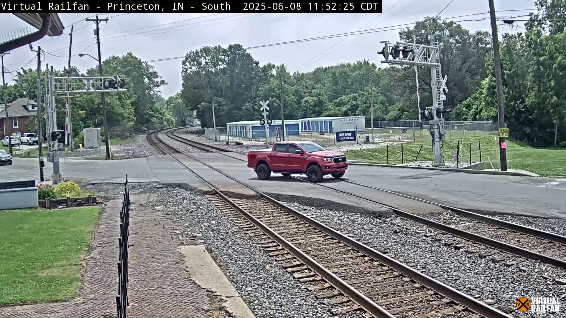 A red pickup truck is crossing a railroad intersection on a partly cloudy day.