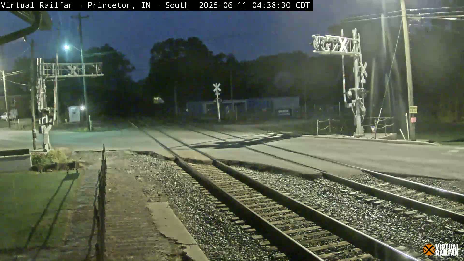 A nighttime view of a railroad crossing with train tracks intersecting a road under dark, clear skies.