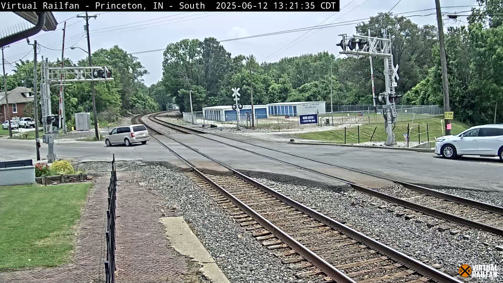 A train crossing with a minivan and an SUV visible, under a partly cloudy sky.