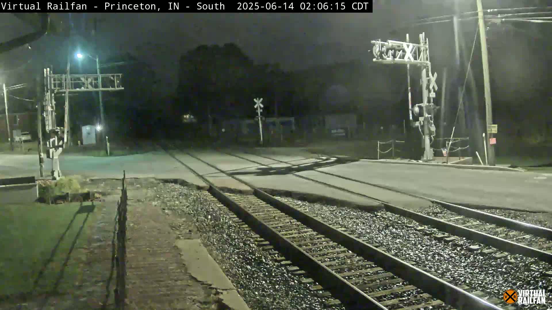 A nighttime view of a railroad crossing with two sets of train tracks intersecting a road, under dark skies.