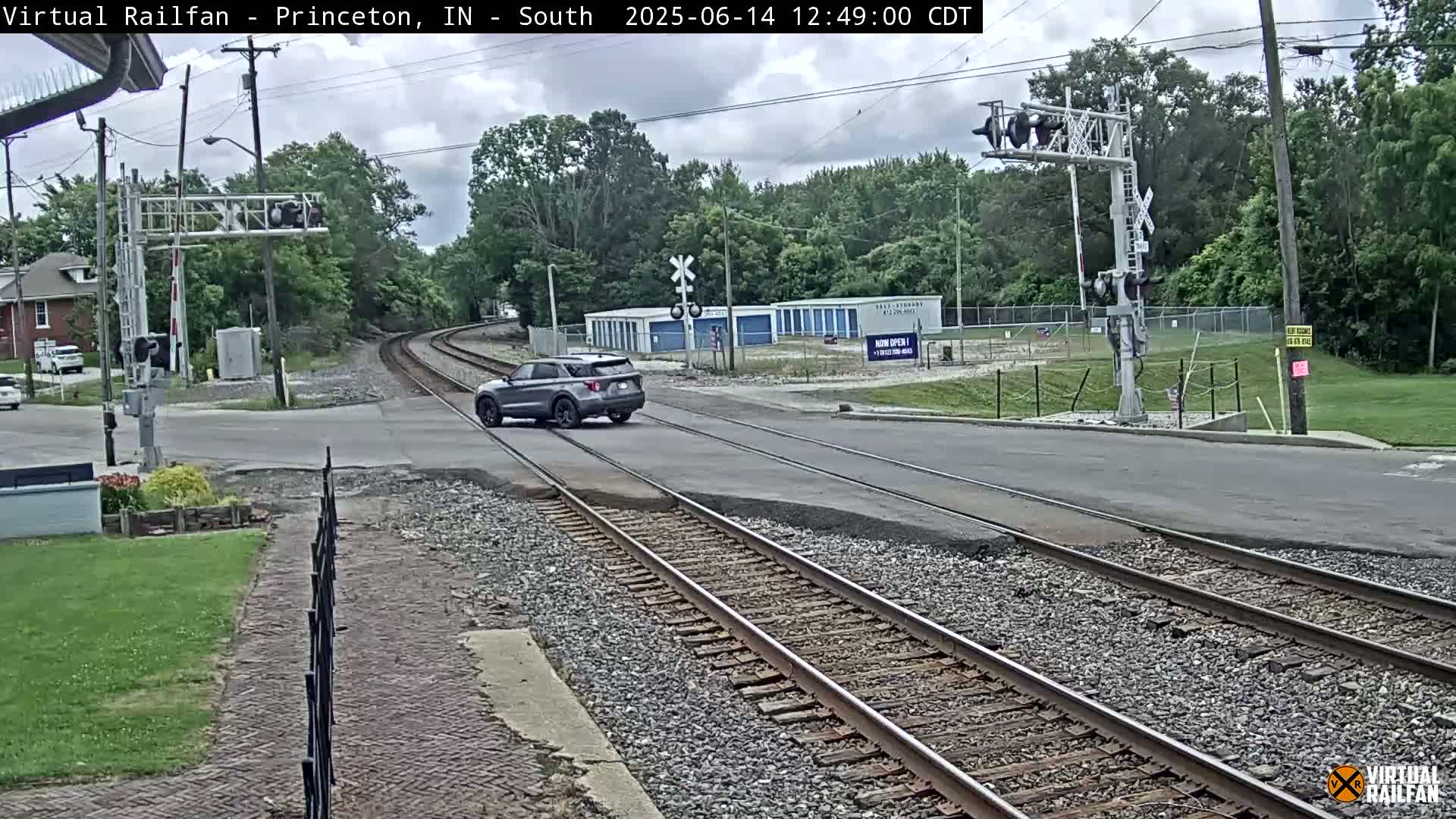 A gray SUV drives across a road that intersects with railroad tracks under a partly cloudy sky.