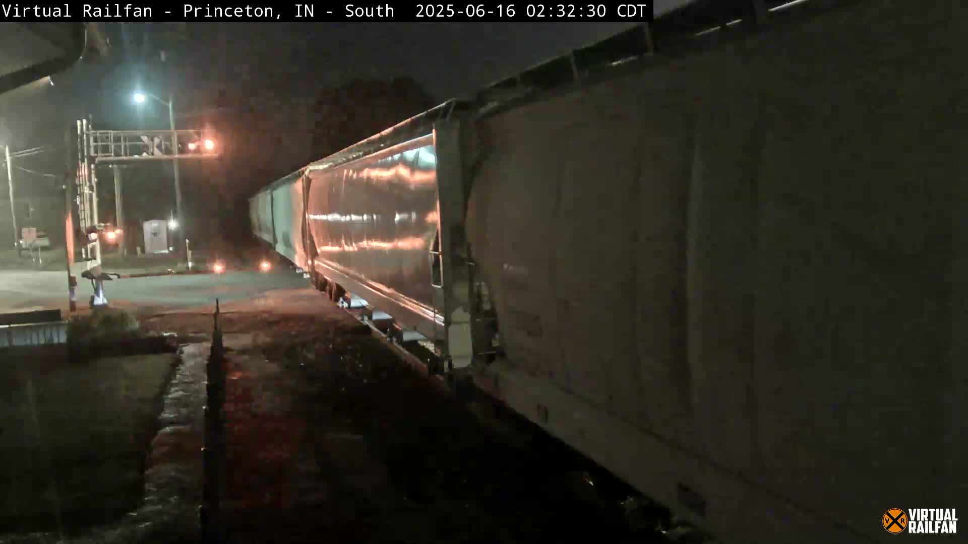 A long freight train passes a railroad crossing at night under dark conditions.