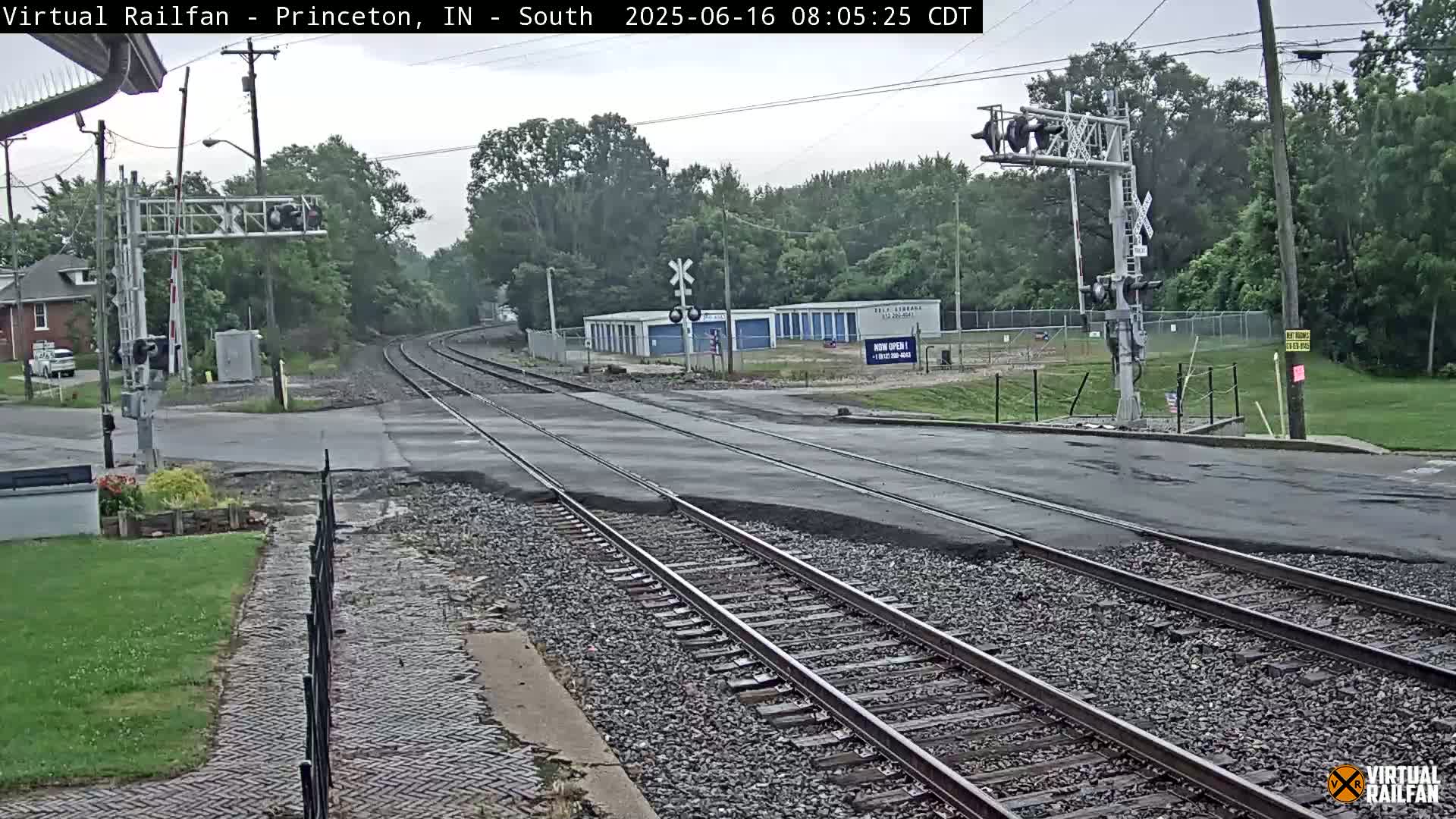 A railroad crossing with train tracks intersecting a road under an overcast sky.