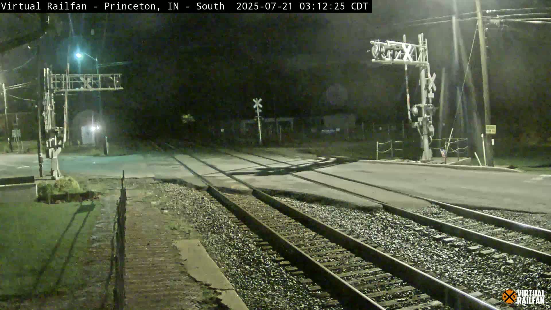 A nighttime view of a railroad crossing with train tracks intersecting a road, under dark, clear skies.