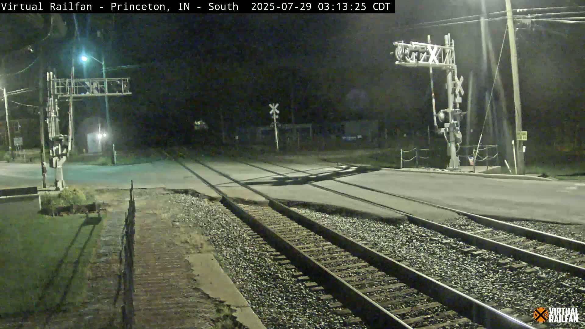 A nighttime view of a railroad crossing with a road intersecting the tracks, illuminated by streetlights.