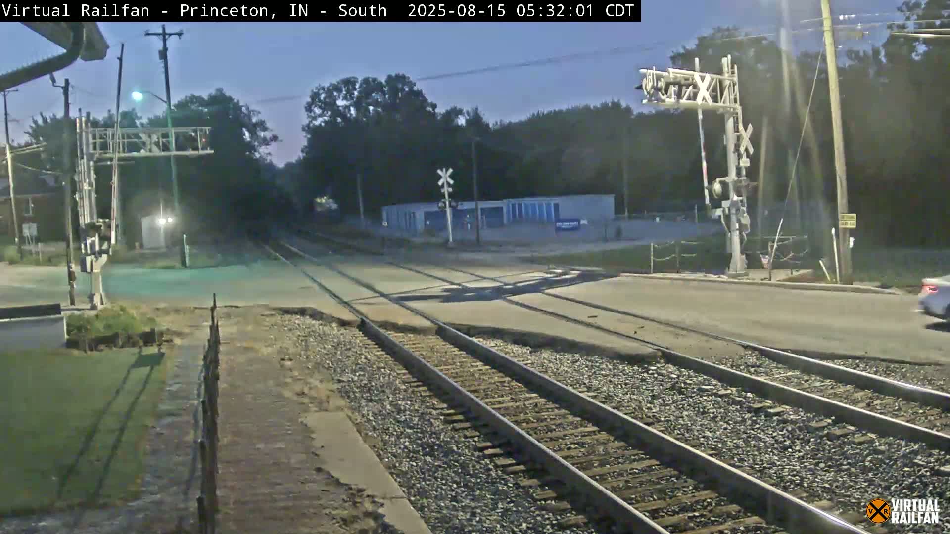 A nighttime view of a railroad crossing with a road intersecting the tracks, illuminated by streetlights.